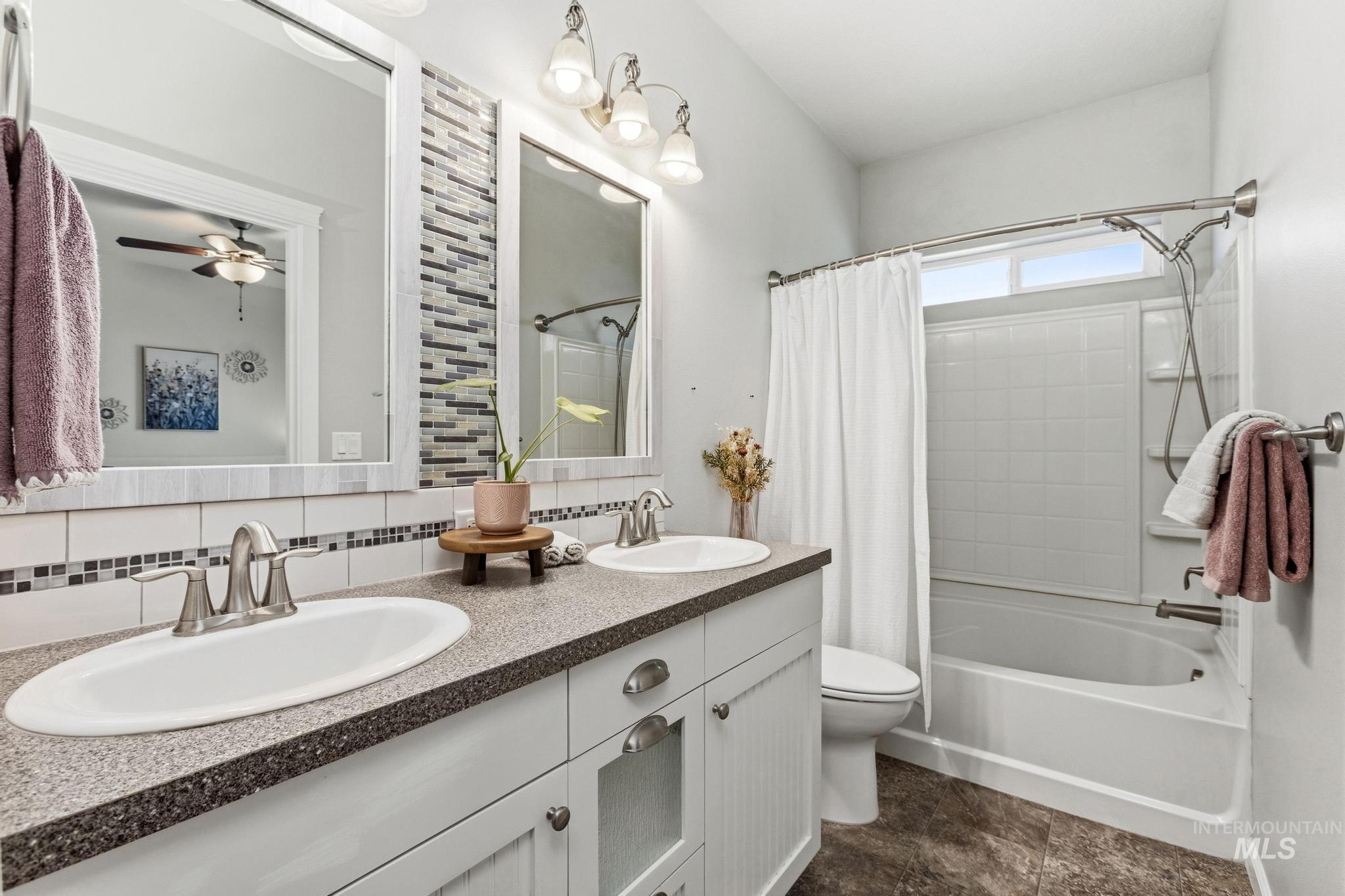 Bathroom with double vanity, decorative backsplash, shower / bathtub combination with curtain, and ceiling fan