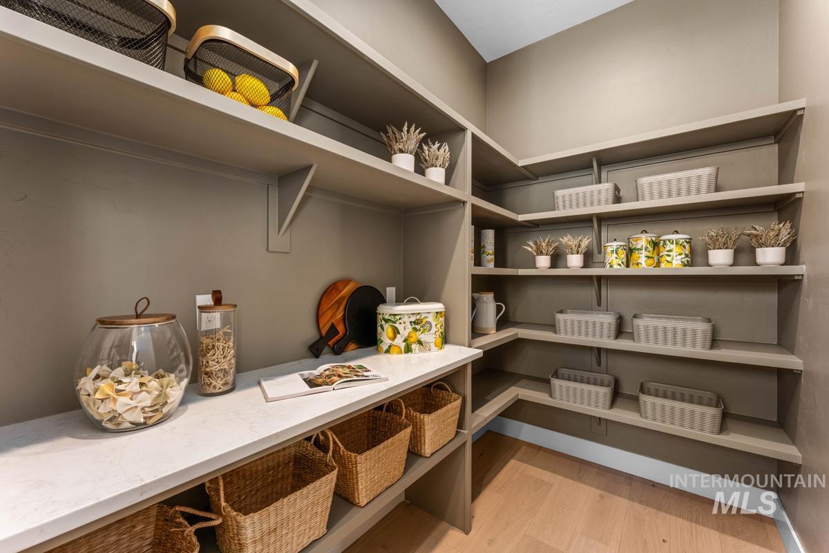 Expansive pantry featuring extensive built-in shelving, a dedicated countertop workspace, integrated storage cubbies, corner shelving, and wood-finish flooring