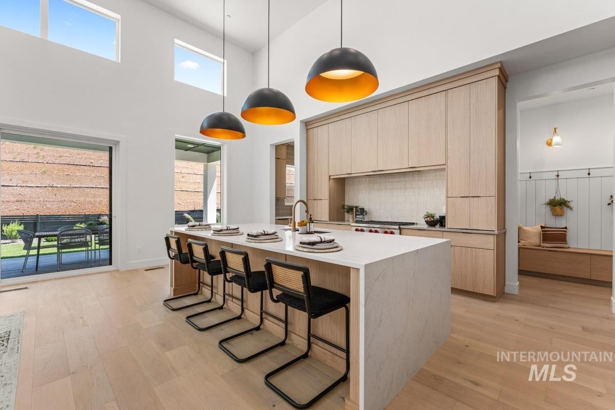 Modern kitchen with a large central island featuring a light-toned countertop, wood-finish cabinetry, a white tiled backsplash, and three contemporary dome pendant lights