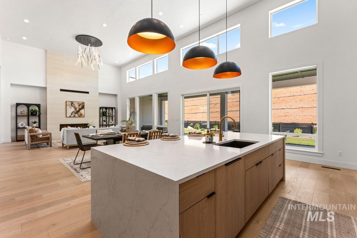 Open-concept living space featuring a waterfall island with a sink, light wood-finish flooring, a two-story ceiling, a fireplace with a light-toned surround, and expansive windows