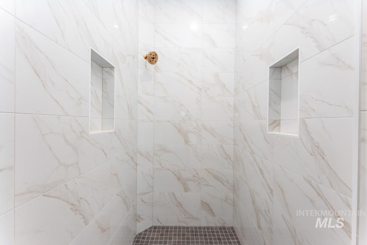 Walk-in shower featuring large format white and gray marble-look wall tiles, dual recessed shower niches, a bronze shower head, and a gray mosaic tile floor