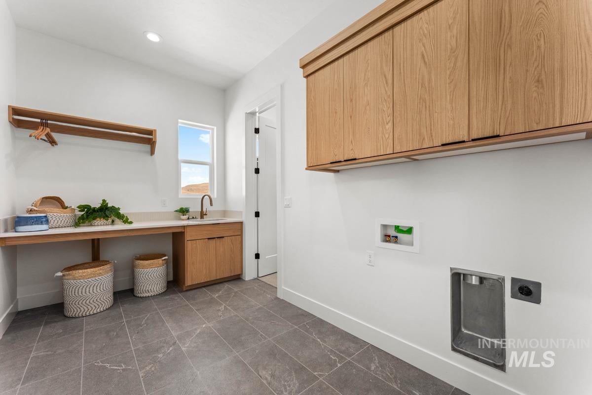 Laundry room featuring a single basin sink with a bronze-finish faucet, under-cabinet storage, wood-finish upper cabinetry, and gray tile flooring