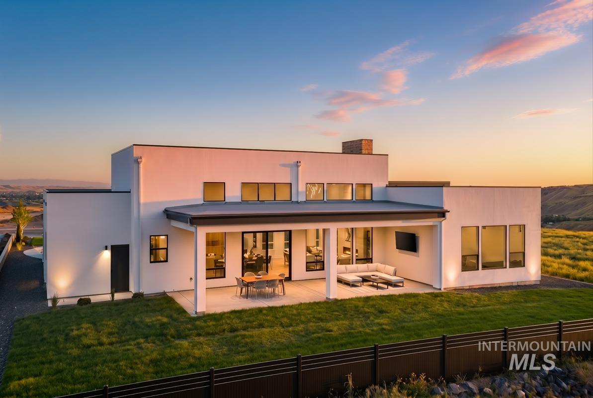 Modern-style stucco exterior featuring a covered patio, multiple large windows, and a manicured lawn