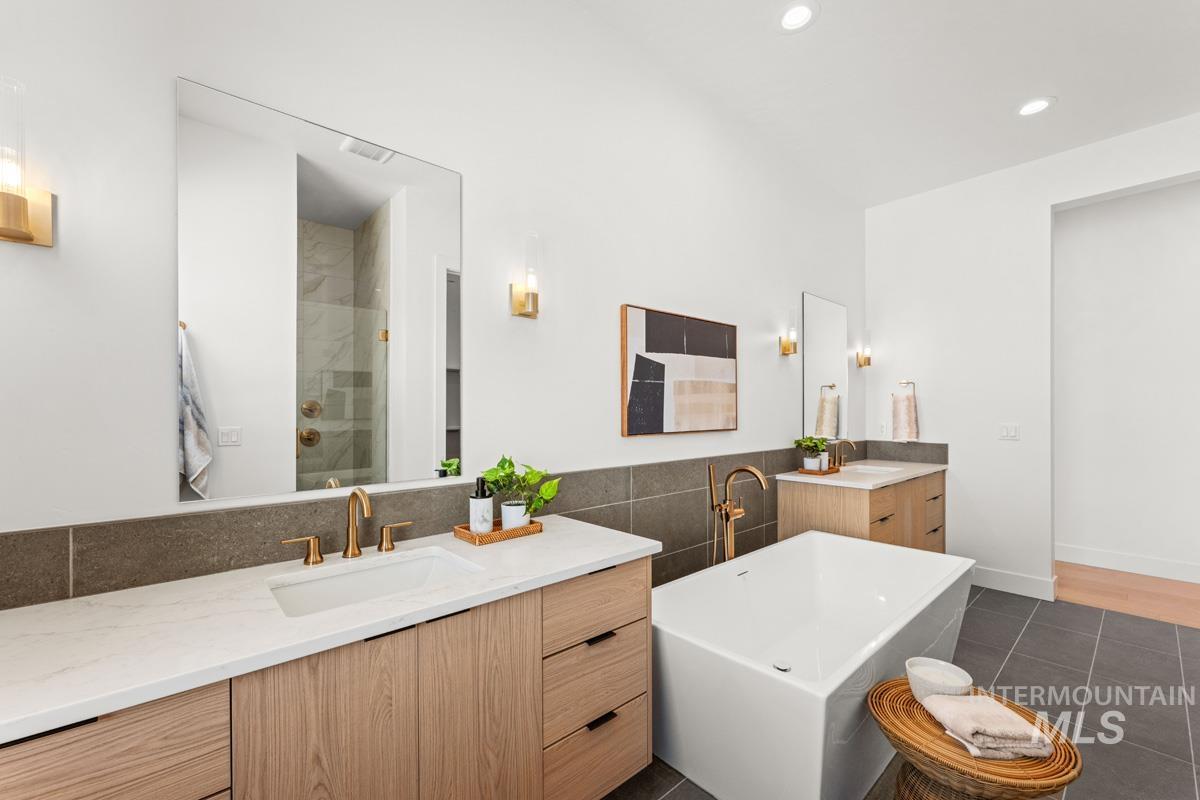 Contemporary bathroom featuring a freestanding tub, dual wood-finish vanities with white countertops, large wall-mounted mirrors, and bronze fixtures