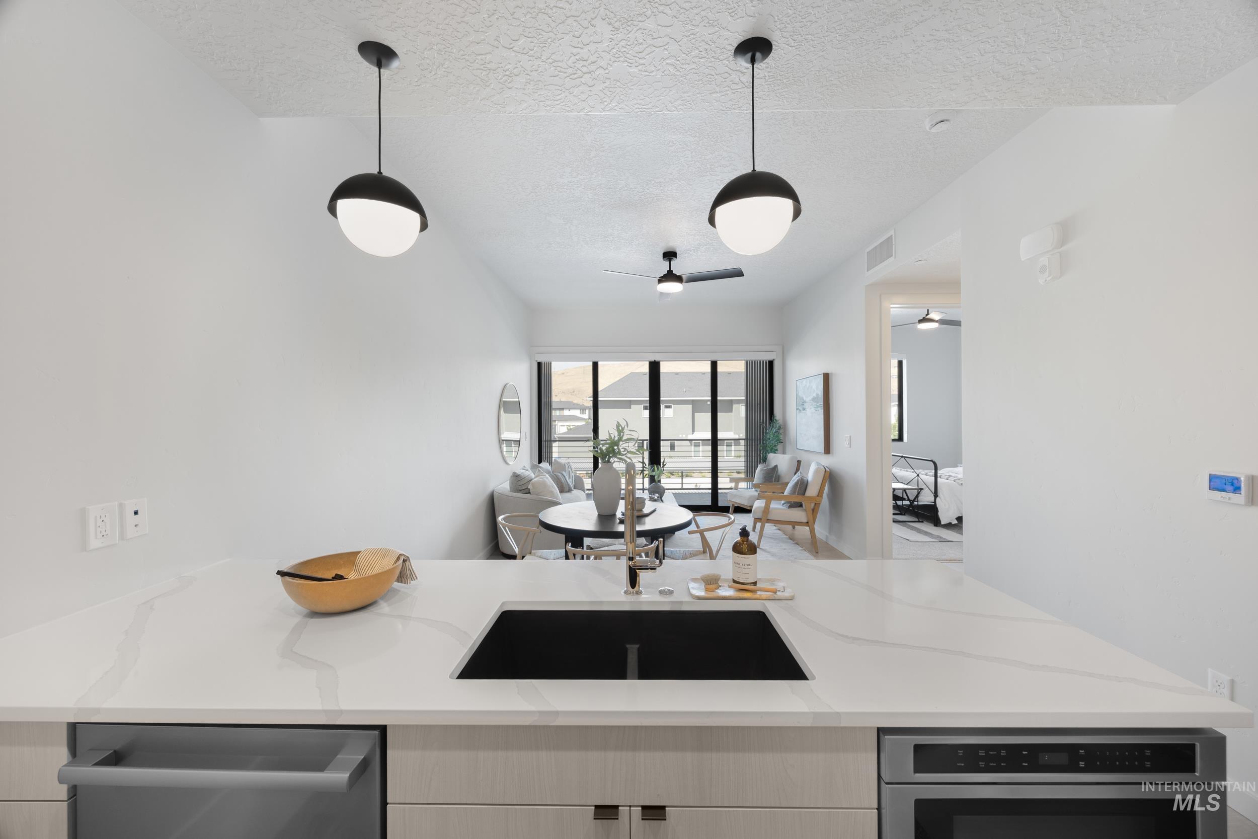 Kitchen featuring open floor plan, light stone countertops, hanging light fixtures, dishwasher, and a textured ceiling