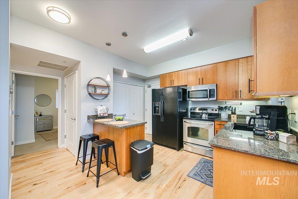 Kitchen featuring stainless steel appliances, a peninsula, light wood-style floors, and a breakfast bar area