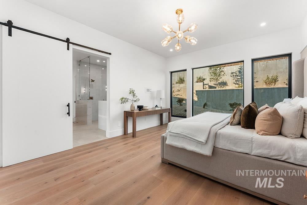 Bedroom featuring light wood-style floors, a barn door, a chandelier, recessed lighting, and connected bathroom