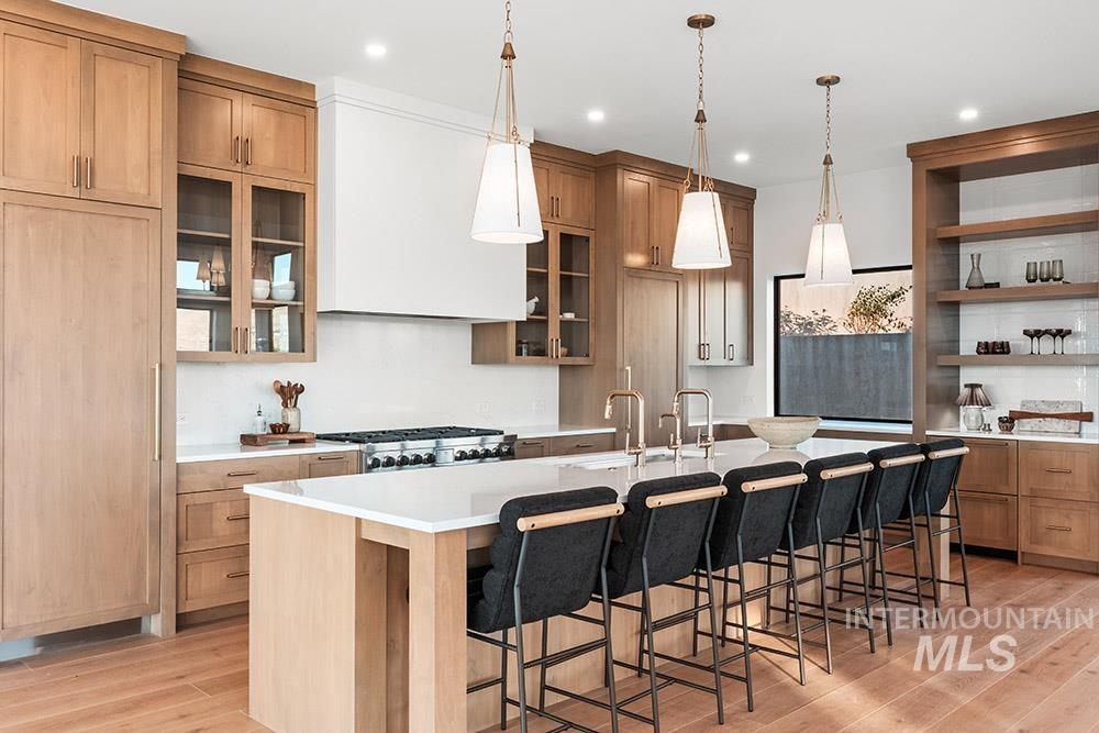 Kitchen featuring a large island with sink, a breakfast bar, light wood-type flooring, pendant lighting, and open shelves