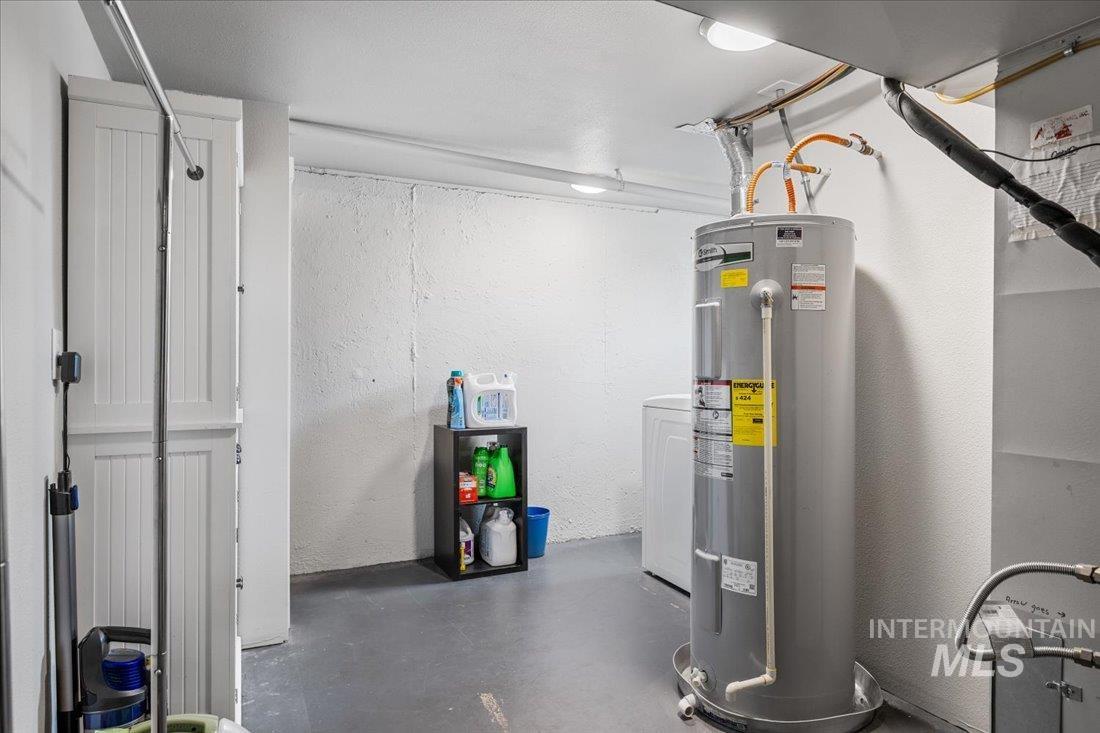 Below grade area with electric water heater, a textured wall, and washer / clothes dryer