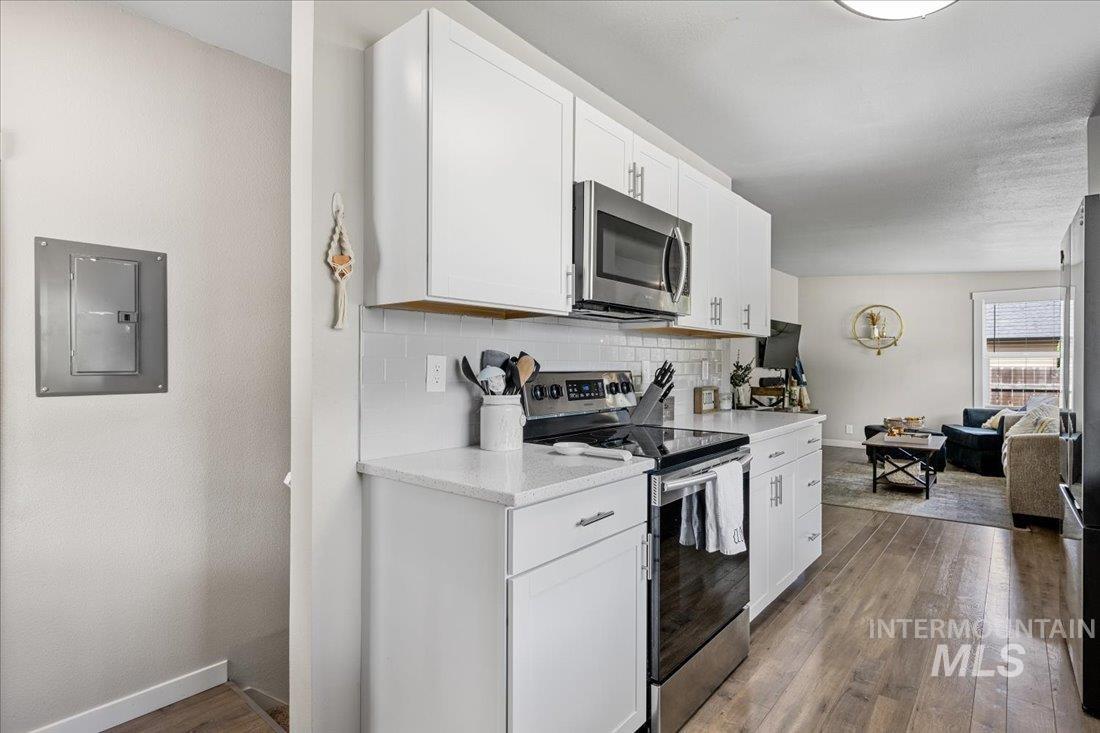 Kitchen with appliances with stainless steel finishes, electric panel, tasteful backsplash, white cabinets, and wood finished floors