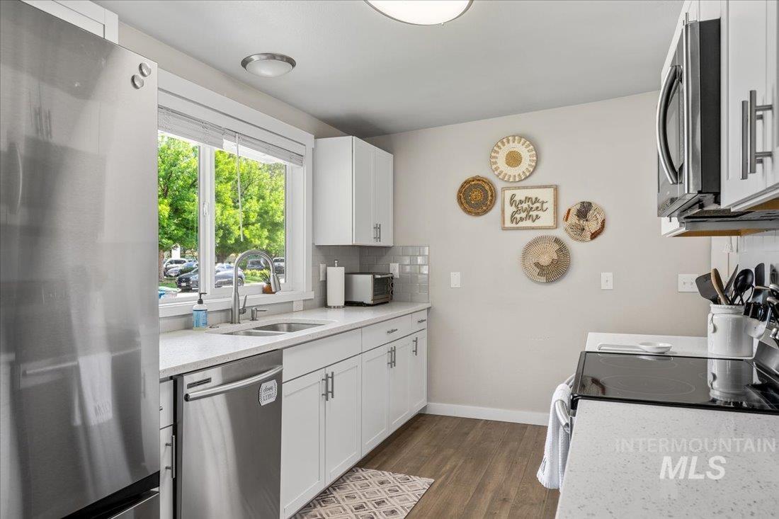 Kitchen with stainless steel appliances, tasteful backsplash, dark wood-style flooring, white cabinetry, and light stone counters
