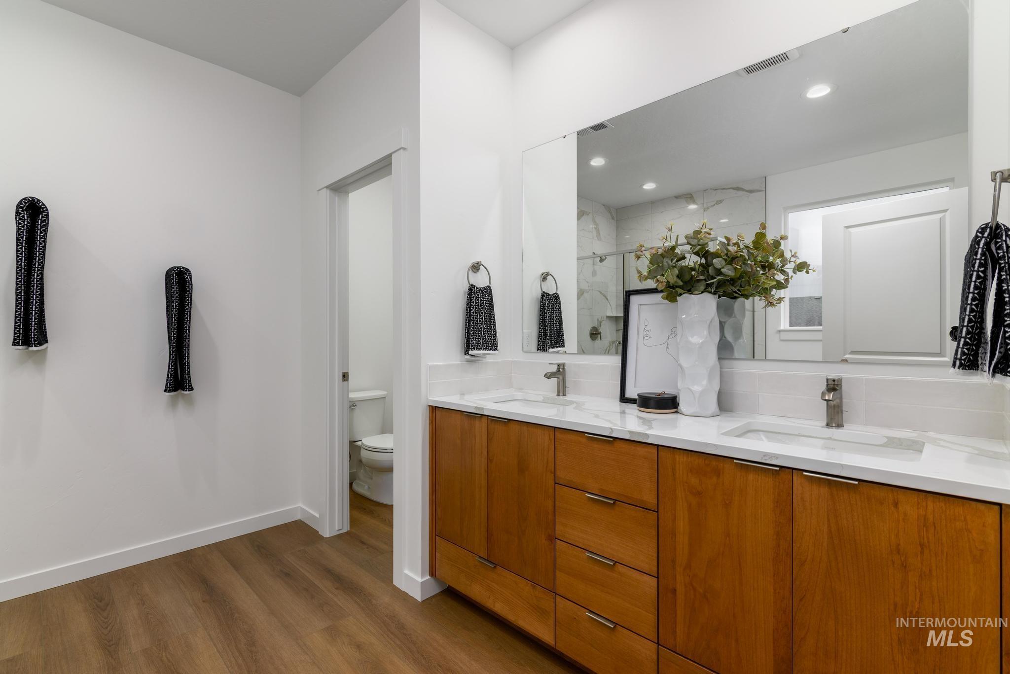 Bathroom featuring a marble finish shower, double vanity, and dark wood-style floors