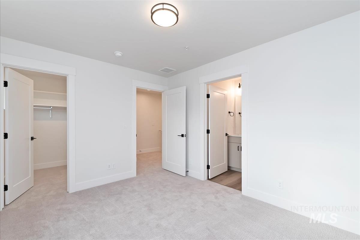 Unfurnished bedroom with a walk in closet, light colored carpet, and ensuite bath