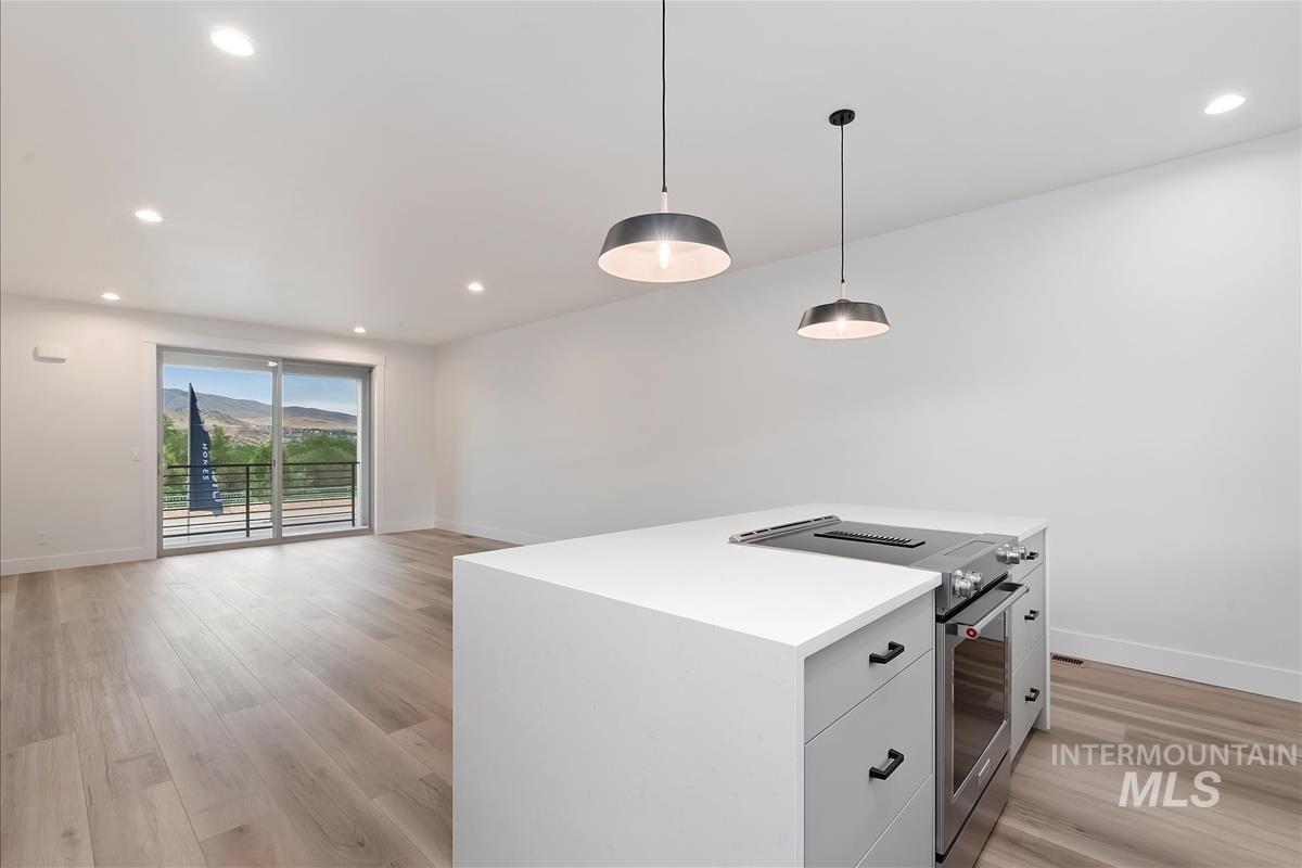 Kitchen featuring stainless steel electric stove, recessed lighting, hanging light fixtures, light wood-type flooring, and white cabinetry