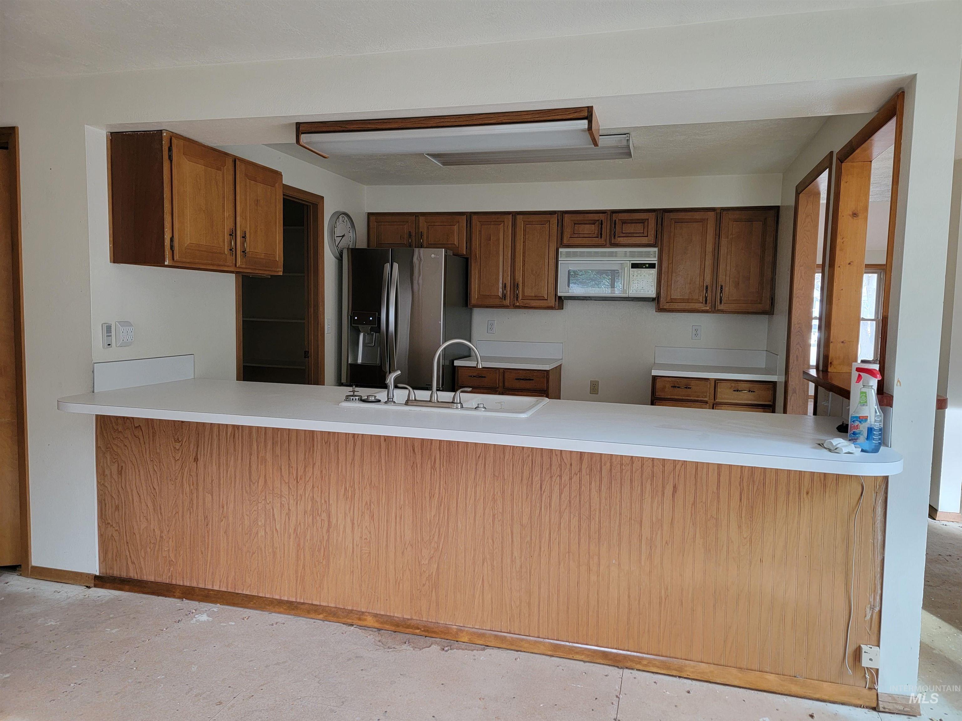 Kitchen featuring brown cabinetry, a peninsula, stainless steel refrigerator with ice dispenser, and white microwave