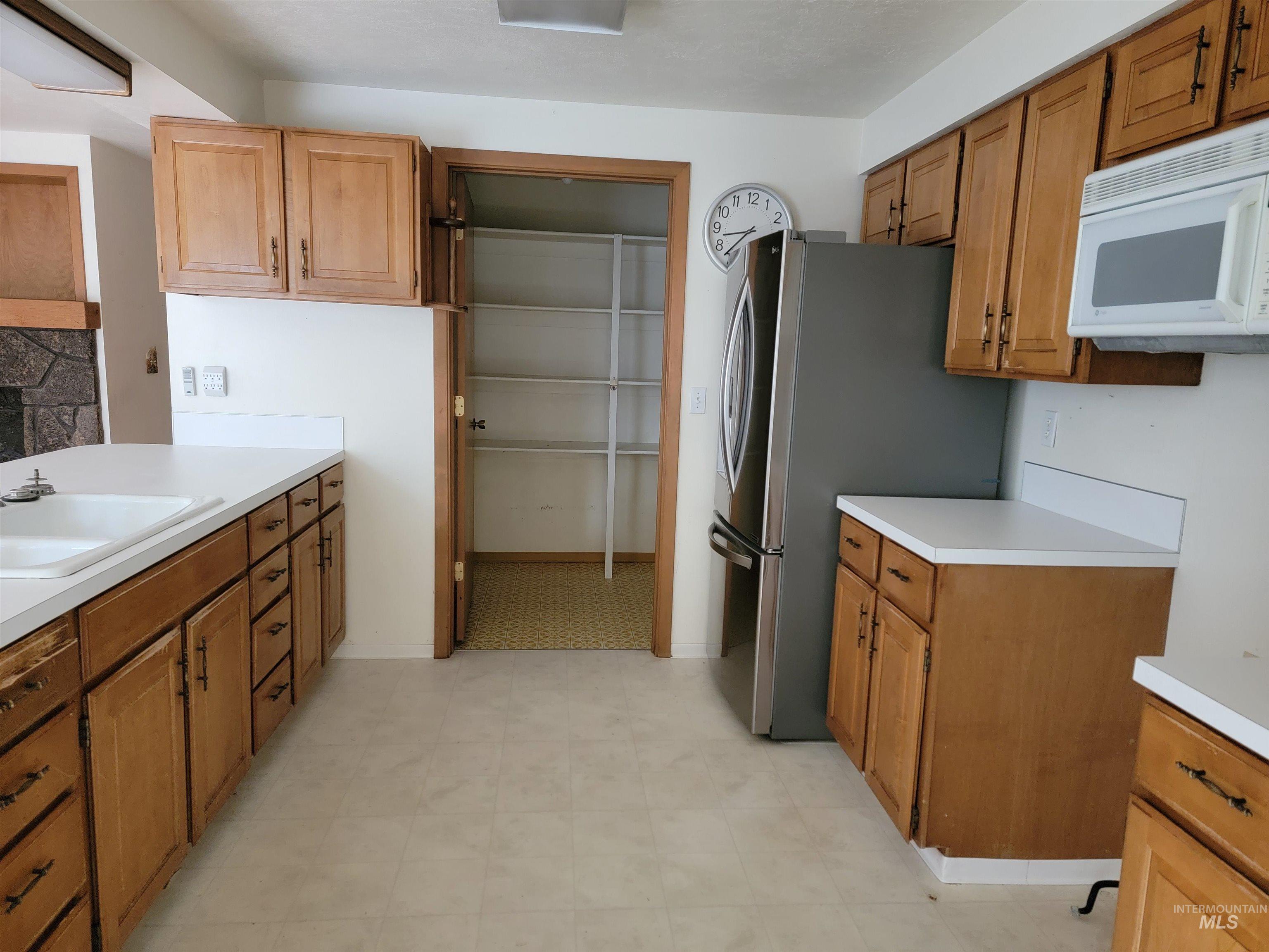 Kitchen with light countertops, white microwave, freestanding refrigerator, and light floors