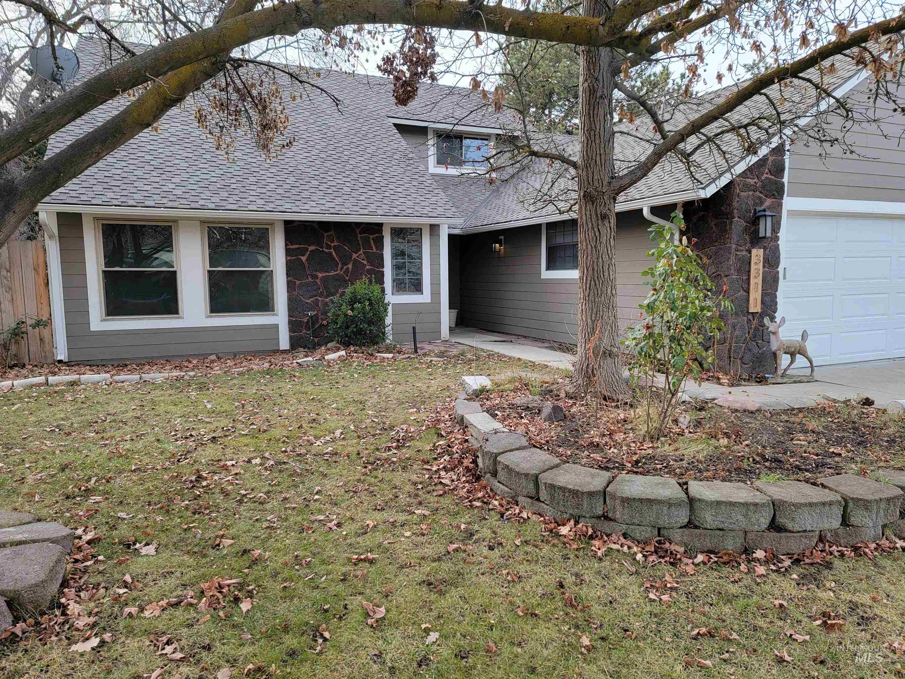 View of front of property featuring stone siding, a shingled roof, a front yard, and an attached garage