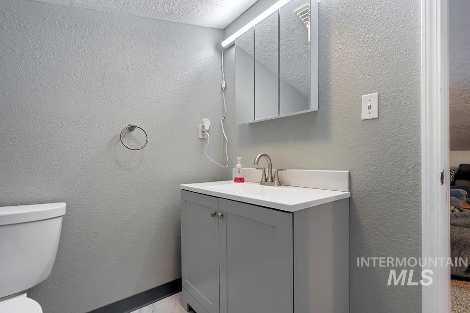 Half bathroom with a textured wall, vanity, and a textured ceiling