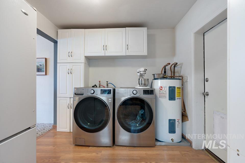 Laundry room with cabinet space, electric water heater, light wood-style floors, and separate washer and dryer