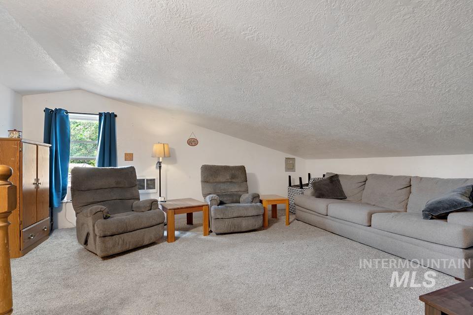 Living room with vaulted ceiling, carpet flooring, and a textured ceiling