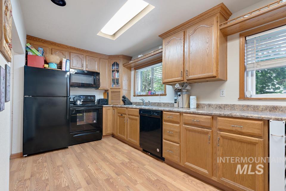 Kitchen featuring black appliances, light countertops, glass insert cabinets, and light wood-style flooring