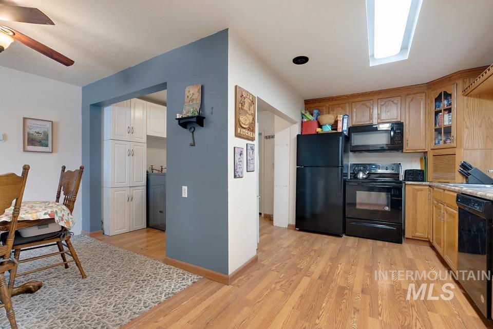 Kitchen with glass insert cabinets, black appliances, light wood-type flooring, and a ceiling fan