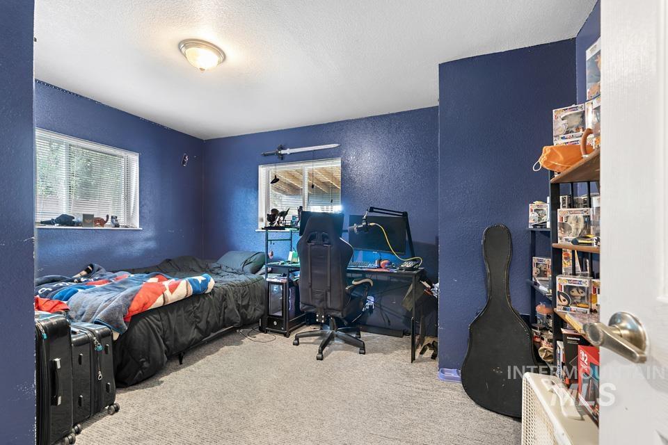 Bedroom with a textured wall, multiple windows, light colored carpet, a textured ceiling, and an office area