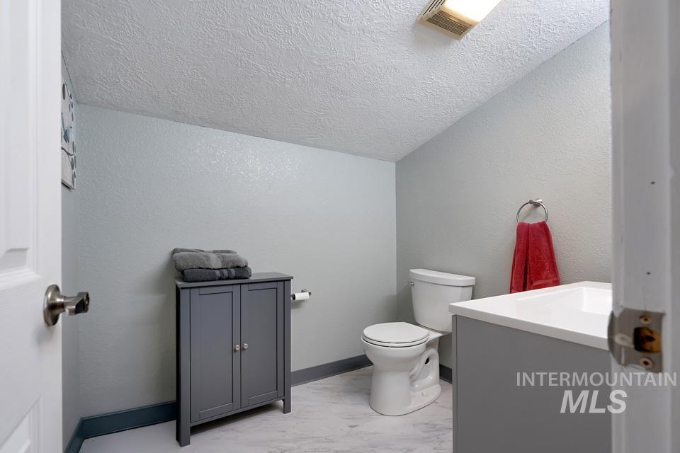 Half bath with a textured wall, vanity, a textured ceiling, and light marble finish flooring