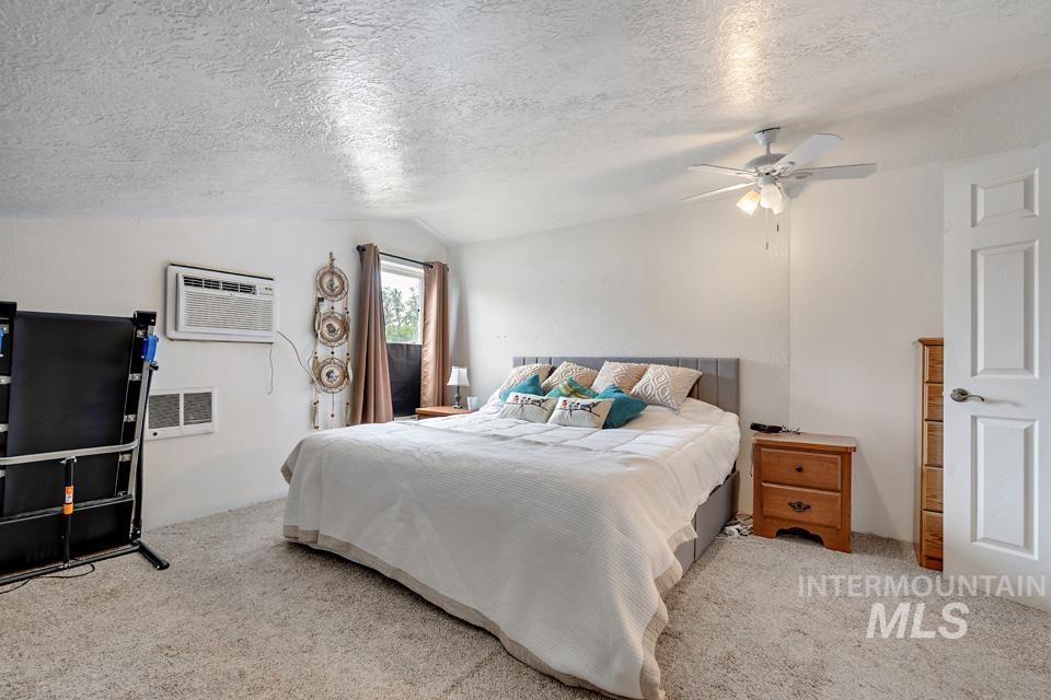 Carpeted bedroom featuring a textured ceiling, lofted ceiling, a wall mounted AC, and ceiling fan