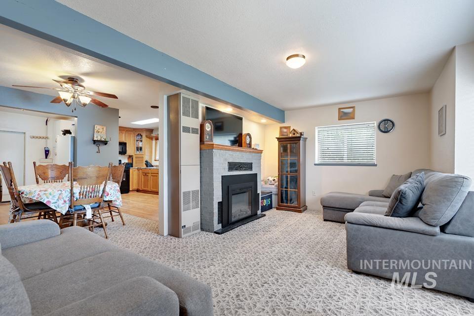 Living room with ceiling fan, a glass covered fireplace, and light carpet