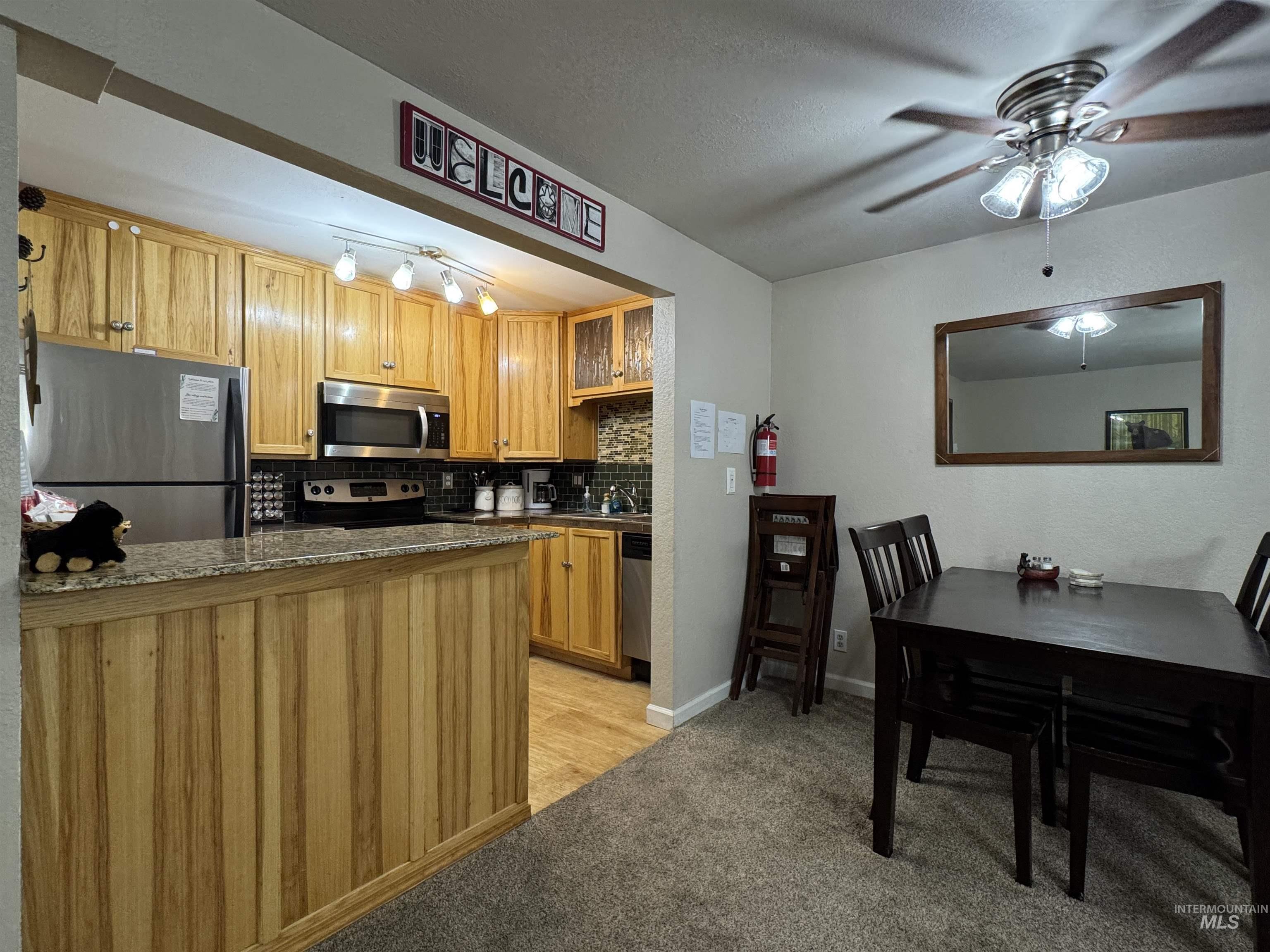 Kitchen with appliances with stainless steel finishes, glass insert cabinets, backsplash, light carpet, and ceiling fan