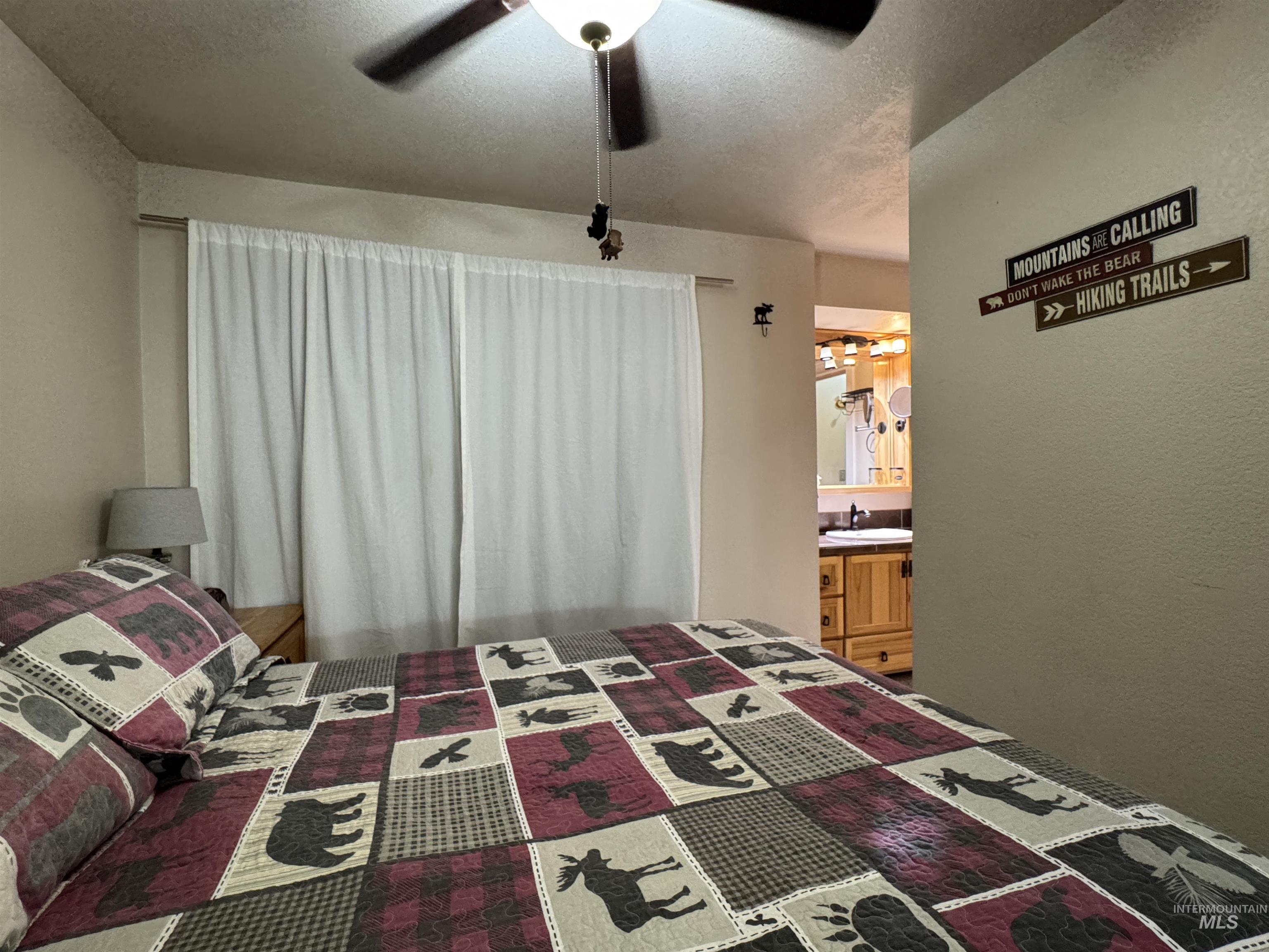 Bedroom with a textured ceiling, ceiling fan, a textured wall, and ensuite bathroom