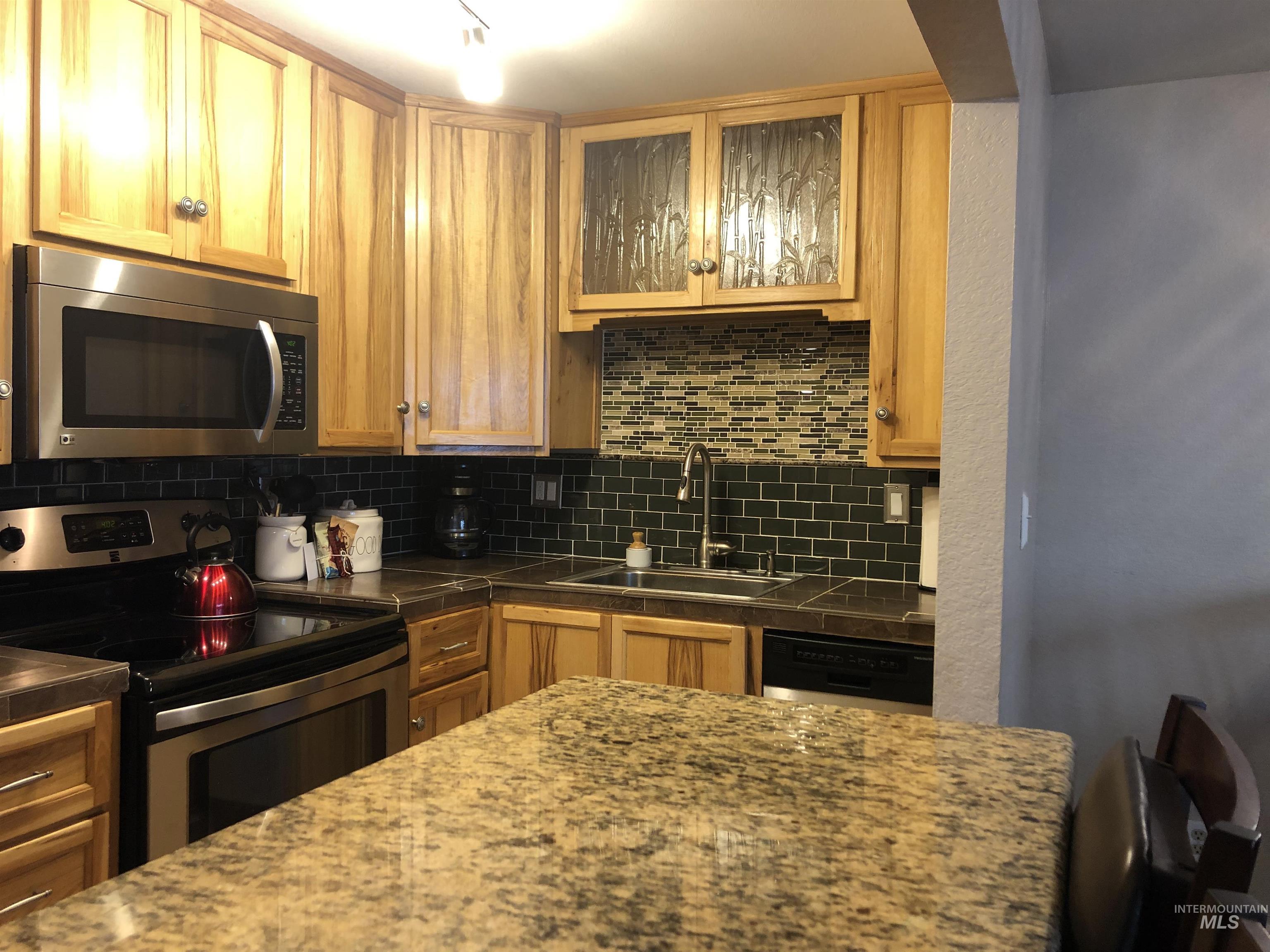 Kitchen with appliances with stainless steel finishes, decorative backsplash, and glass insert cabinets