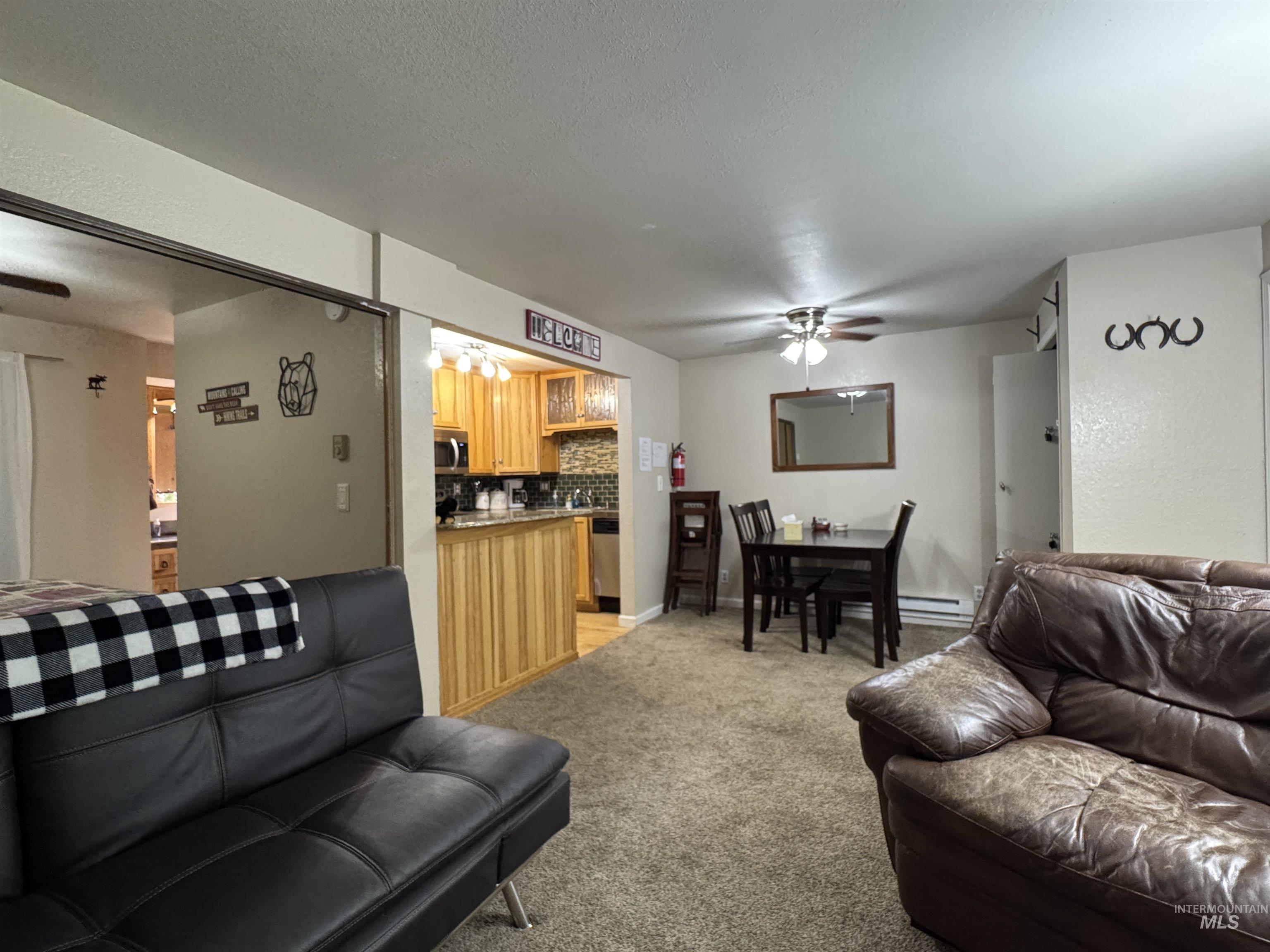 Living area featuring a ceiling fan, light carpet, a baseboard radiator, and a textured ceiling