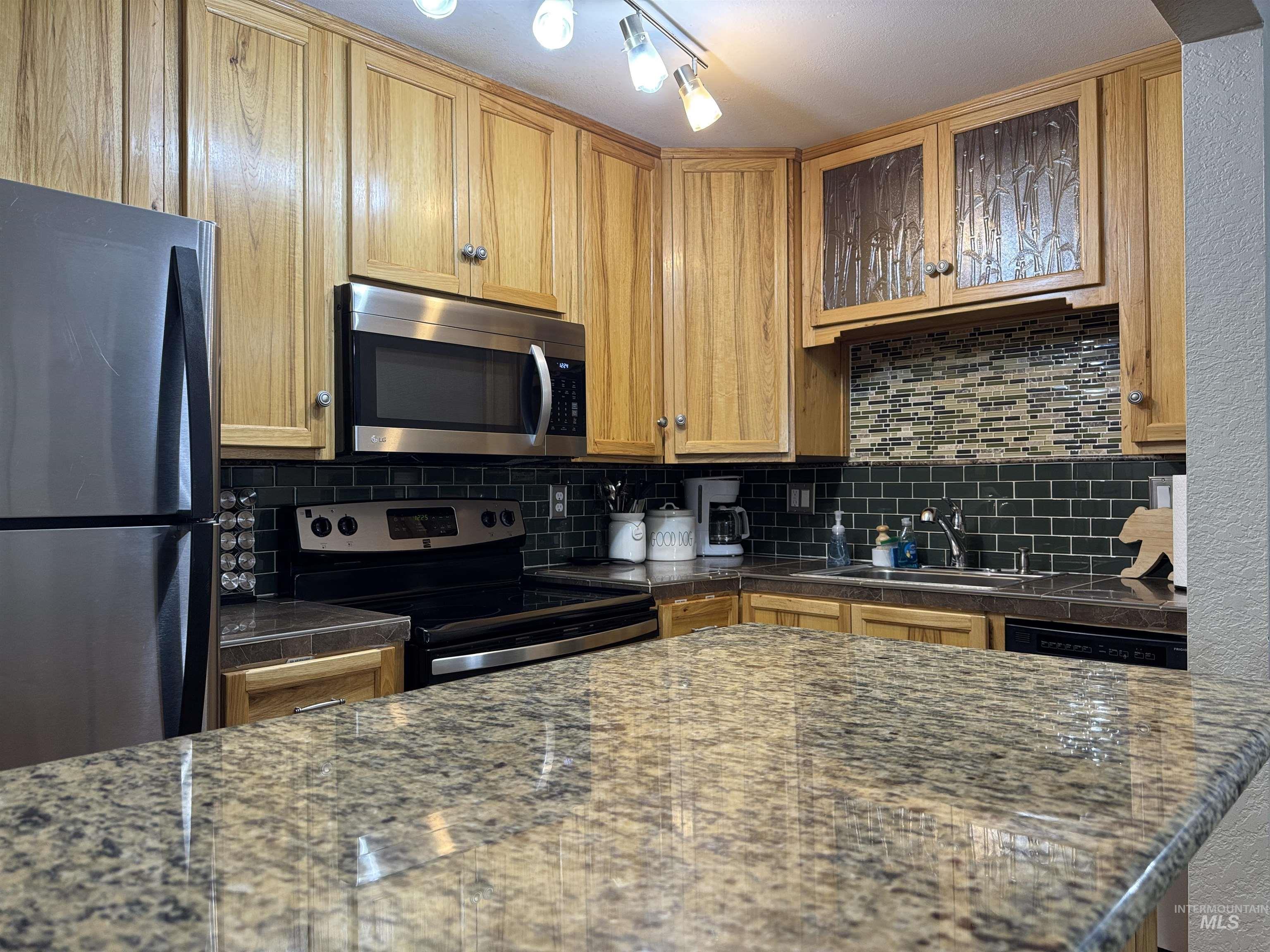 Kitchen featuring appliances with stainless steel finishes, backsplash, brown cabinetry, and glass insert cabinets