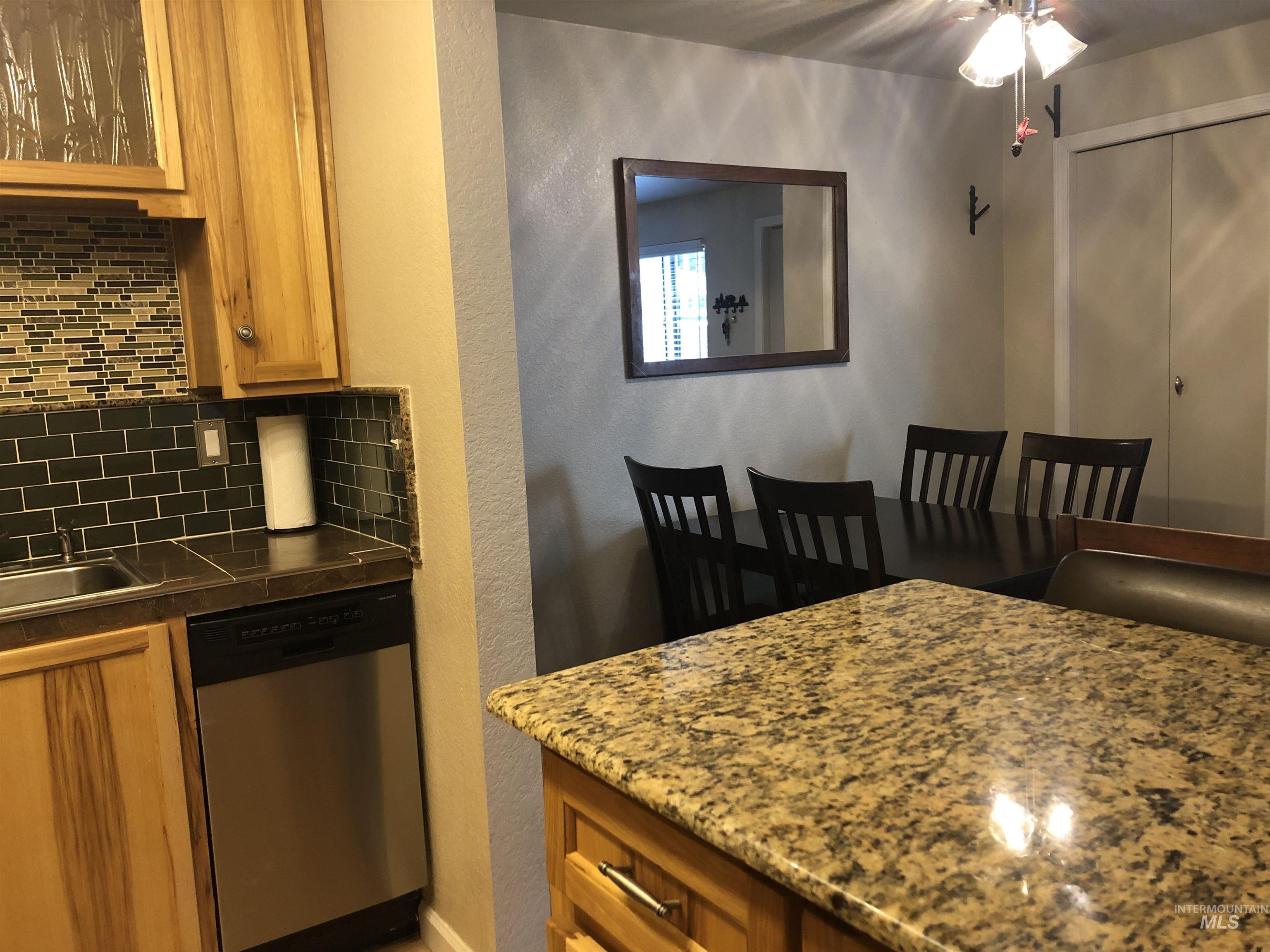 Kitchen with backsplash, a textured wall, brown cabinets, dishwasher, and glass insert cabinets