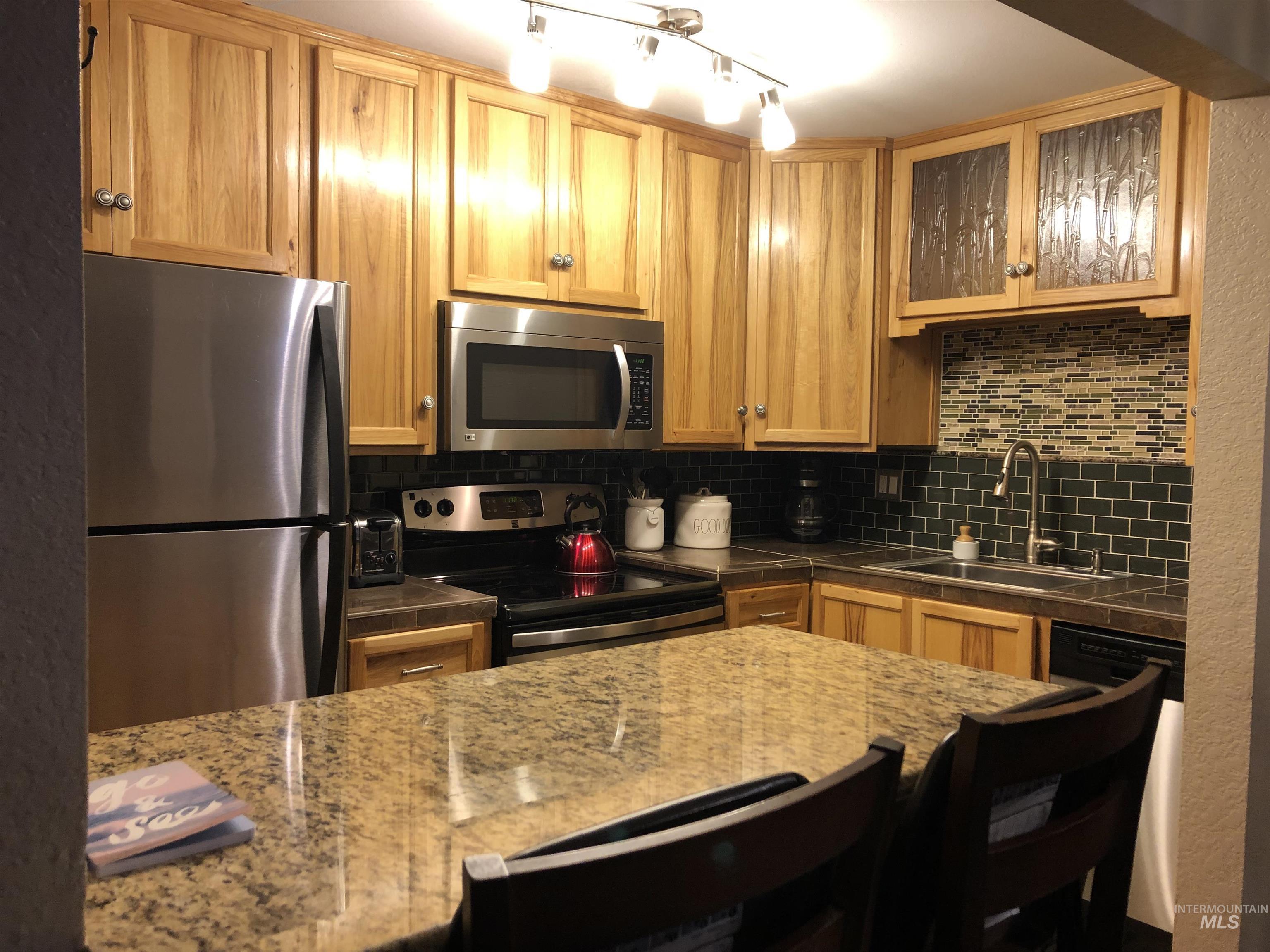 Kitchen featuring appliances with stainless steel finishes, backsplash, and glass insert cabinets