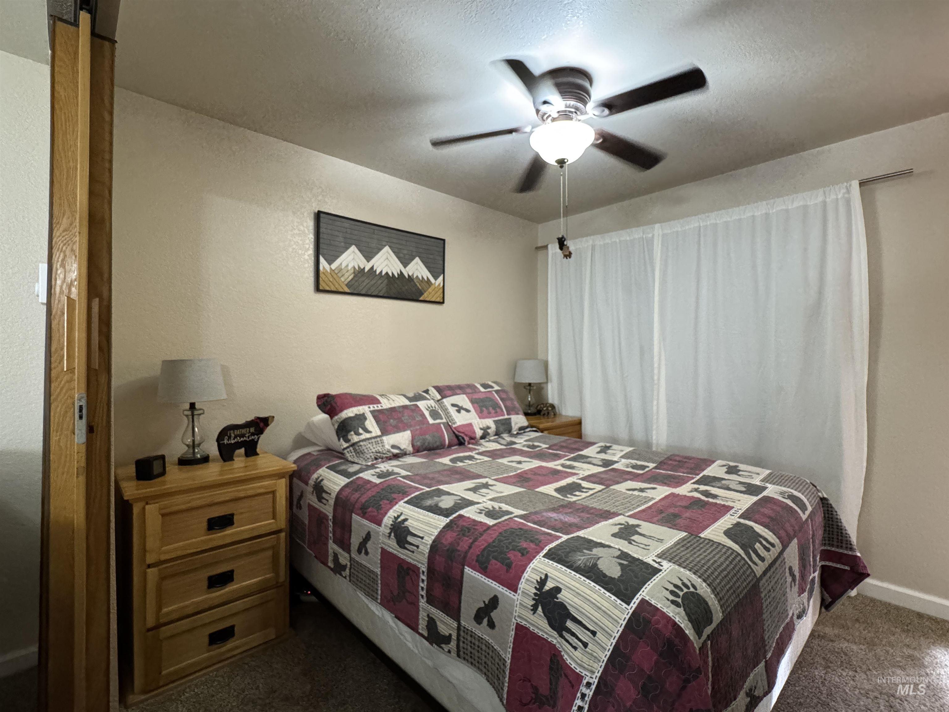 Bedroom with a ceiling fan, dark carpet, a textured ceiling, and a textured wall