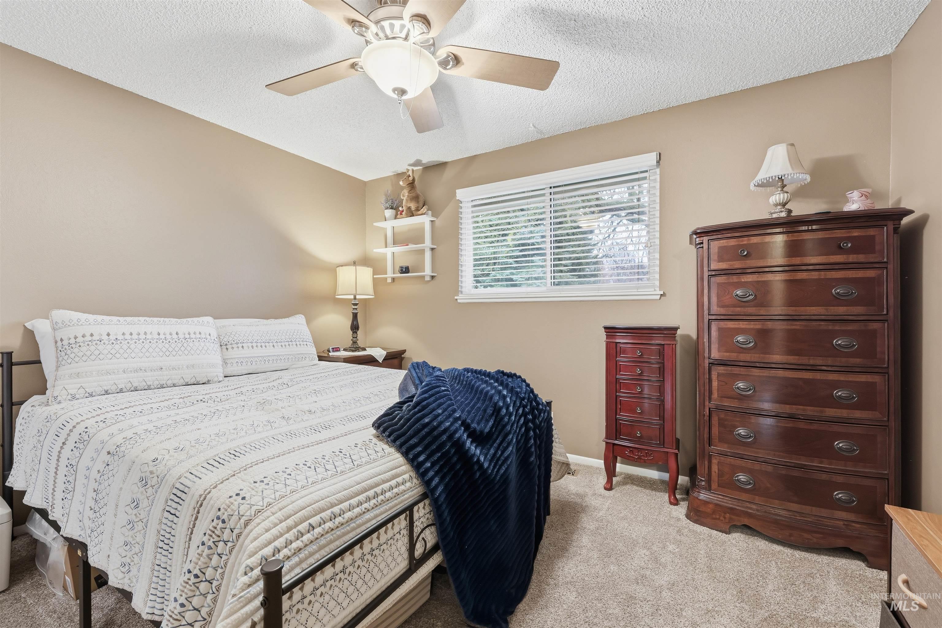 Bedroom with a textured ceiling, light carpet, and a ceiling fan
