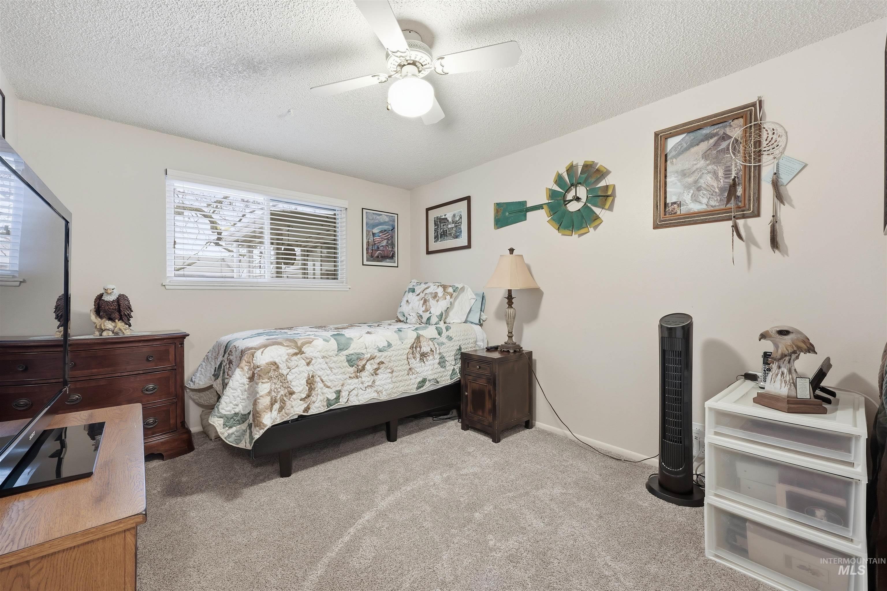 Bedroom with light colored carpet, a textured ceiling, and a ceiling fan