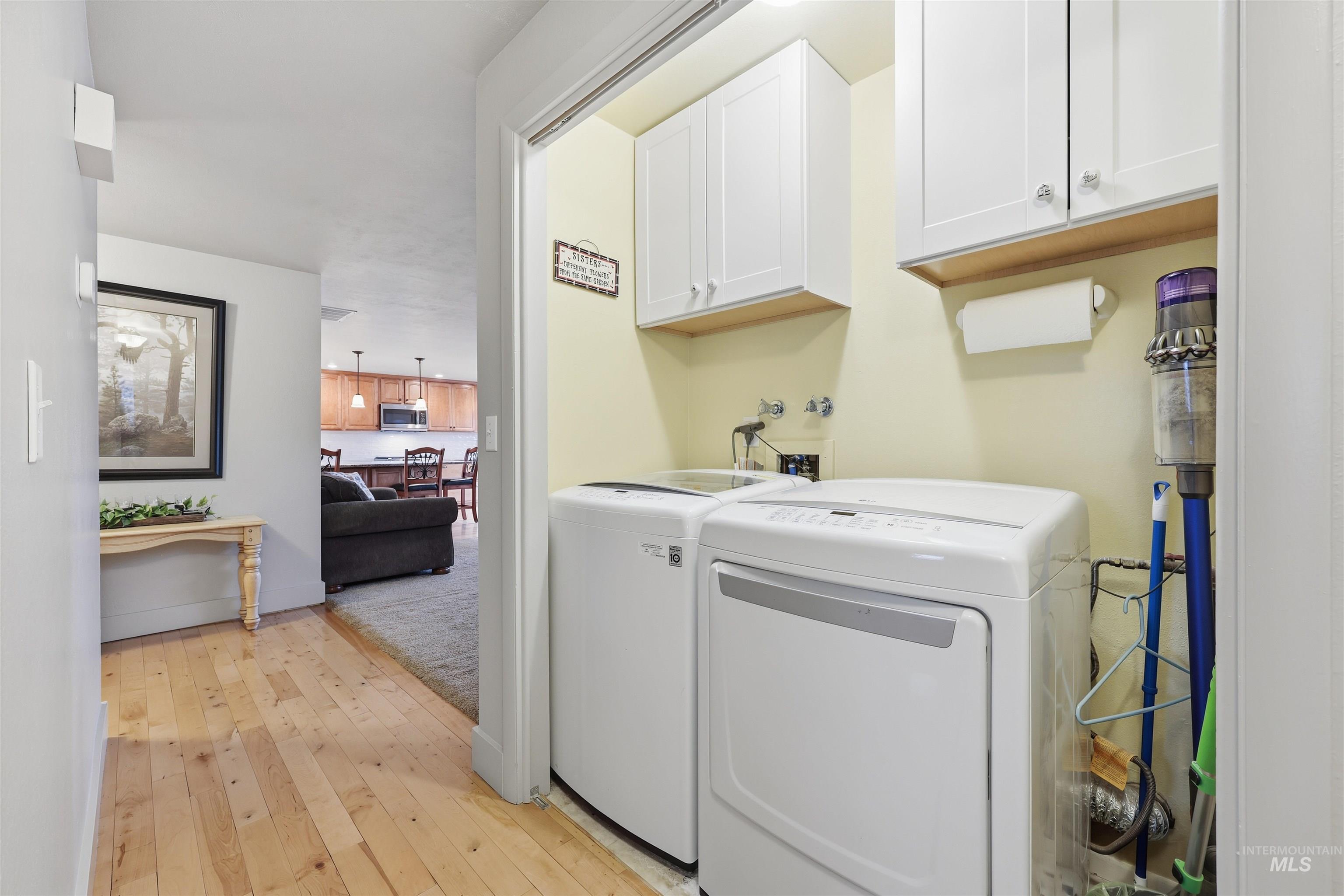 Laundry area with cabinet space, light wood finished floors, and separate washer and dryer