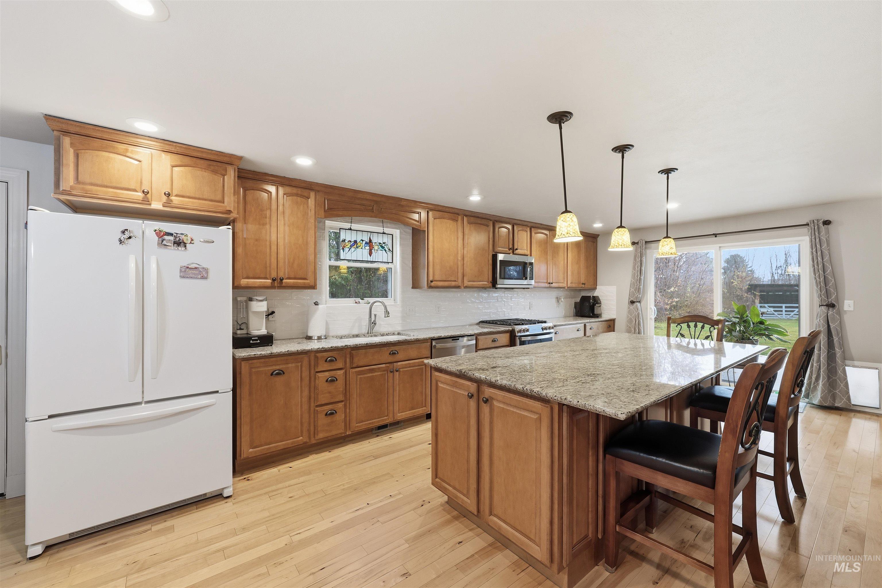 Kitchen with light stone countertops, brown cabinetry, stainless steel appliances, light wood-style flooring, and tasteful backsplash