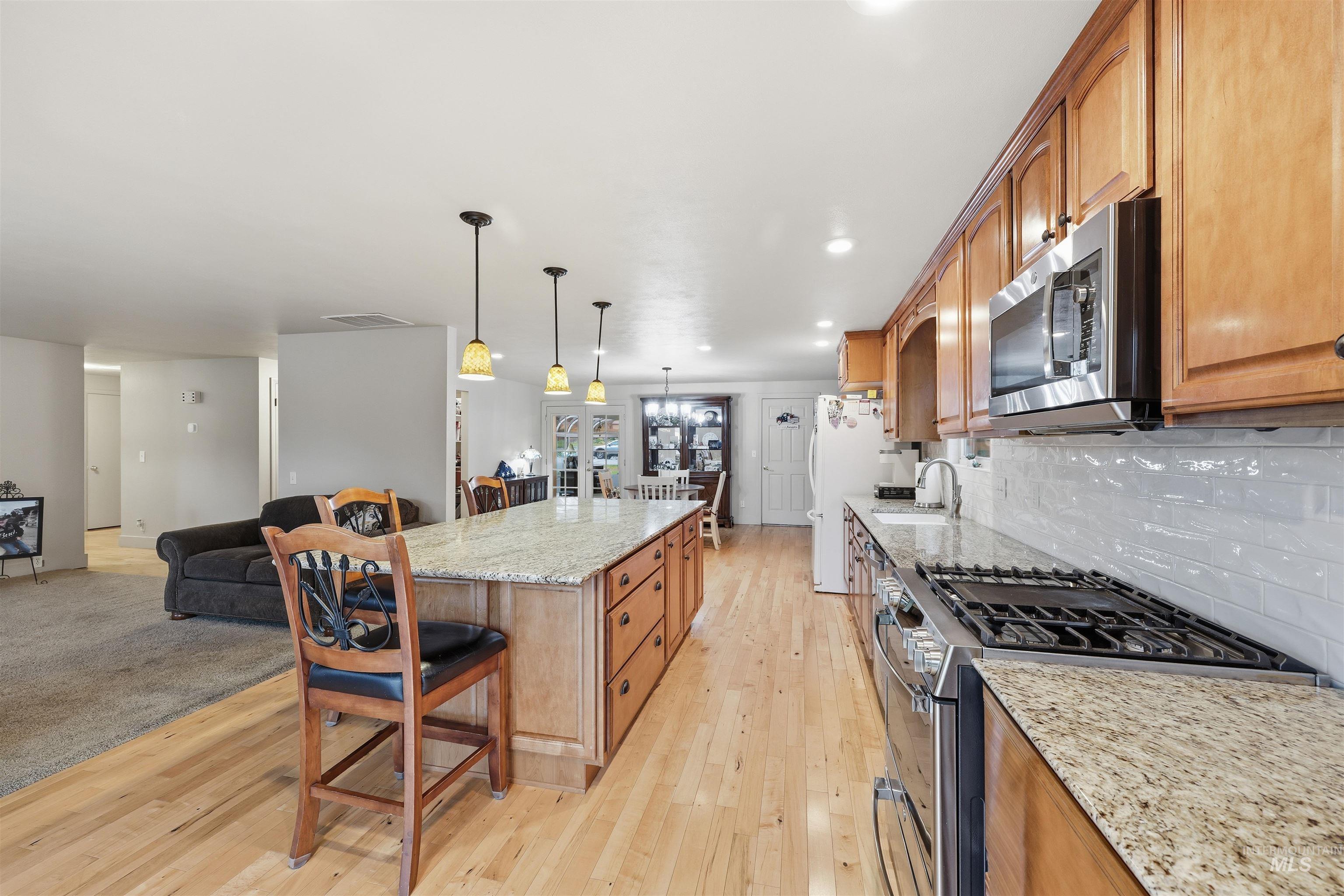 Kitchen featuring a breakfast bar, light Granite countertops, appliances with stainless steel finishes, brown cabinetry, and recessed lighting