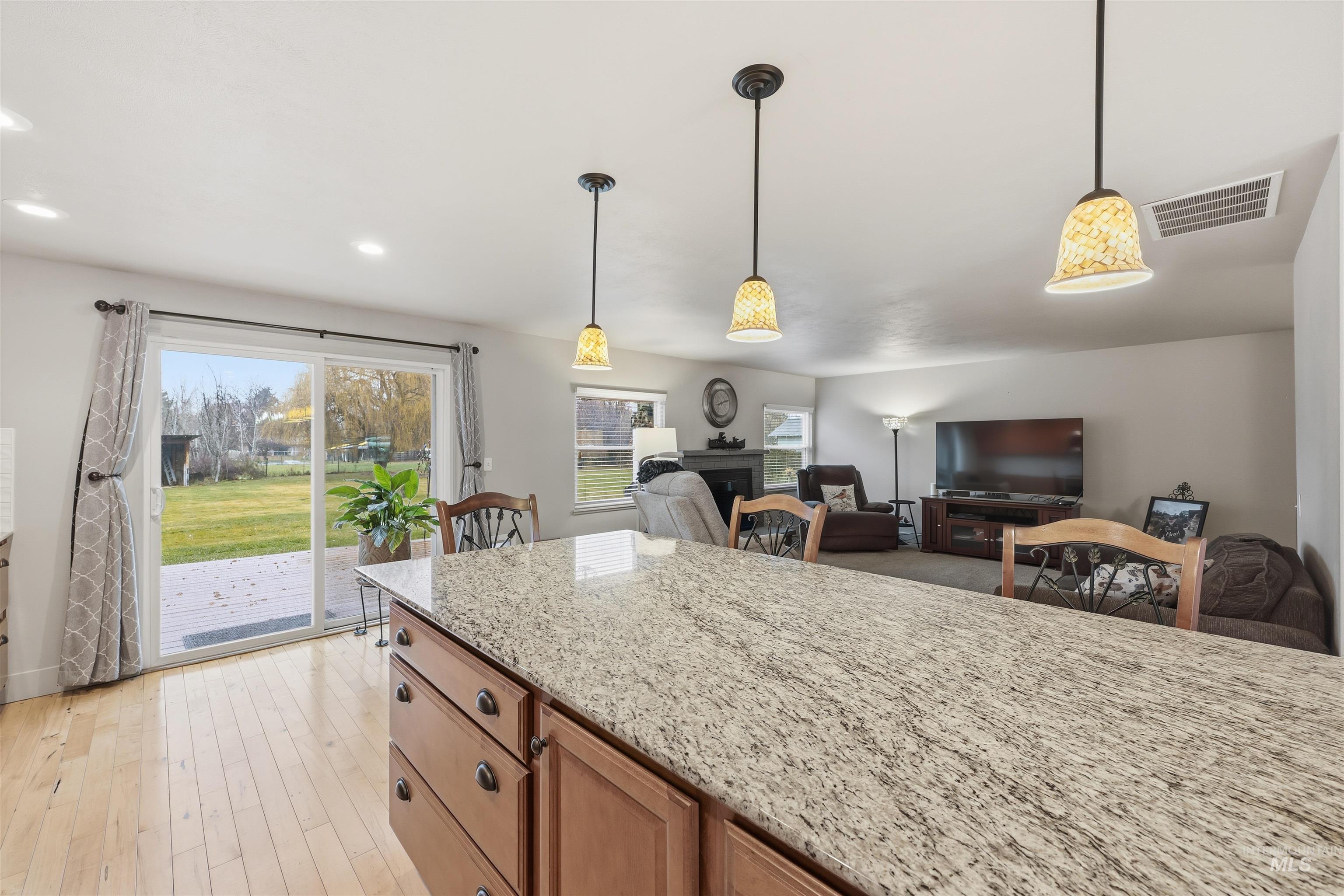 Kitchen featuring a fireplace, light stone counters, pendant lighting, brown cabinets, and recessed lighting