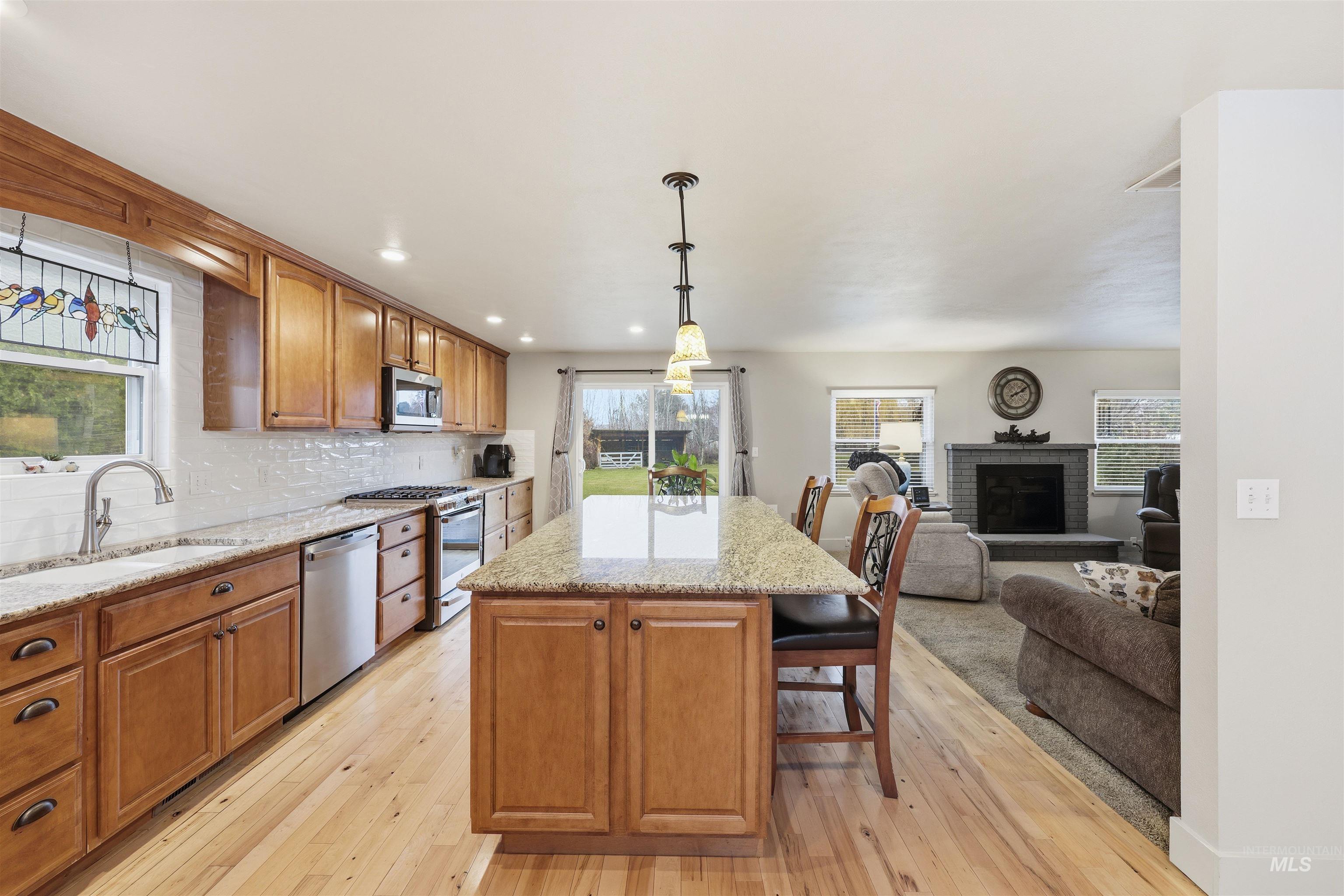 Kitchen with brown cabinets, tasteful backsplash, light stone countertops, pendant lighting, and a breakfast bar