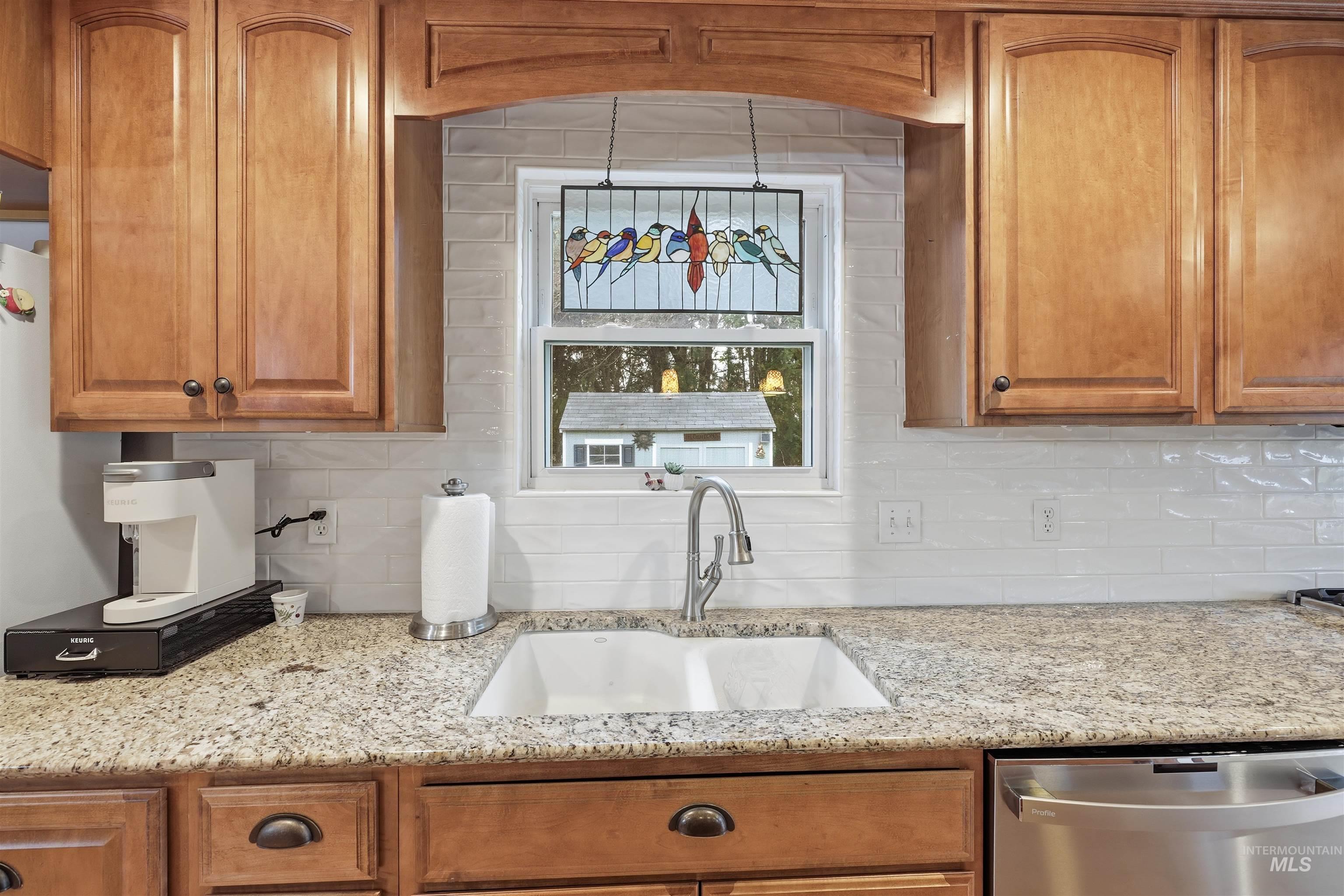Kitchen with brown cabinetry, stainless steel dishwasher, light Granite countertops, and decorative backsplash