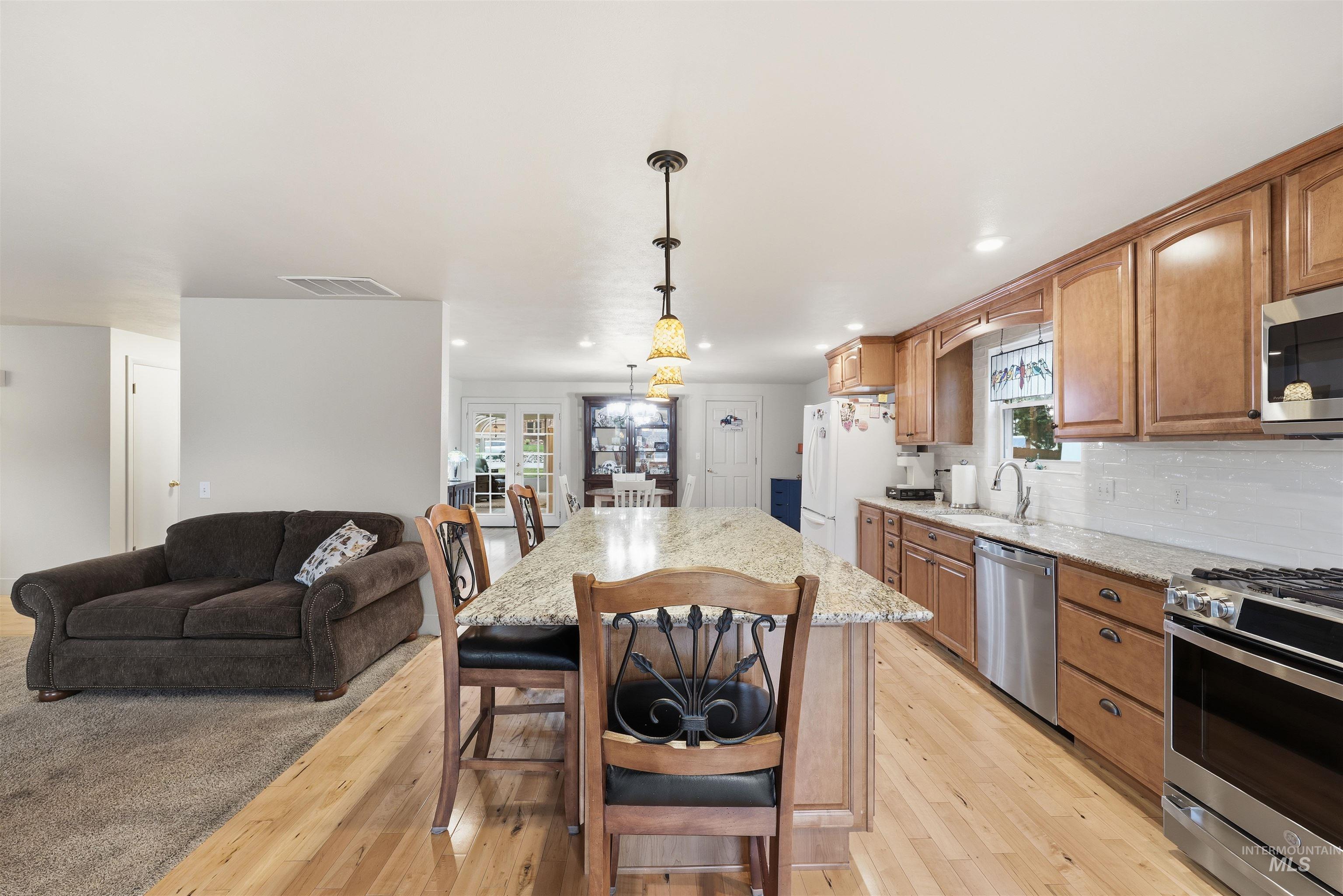 Kitchen featuring a kitchen bar, decorative light fixtures, appliances with stainless steel finishes, open floor plan, and brown cabinetry