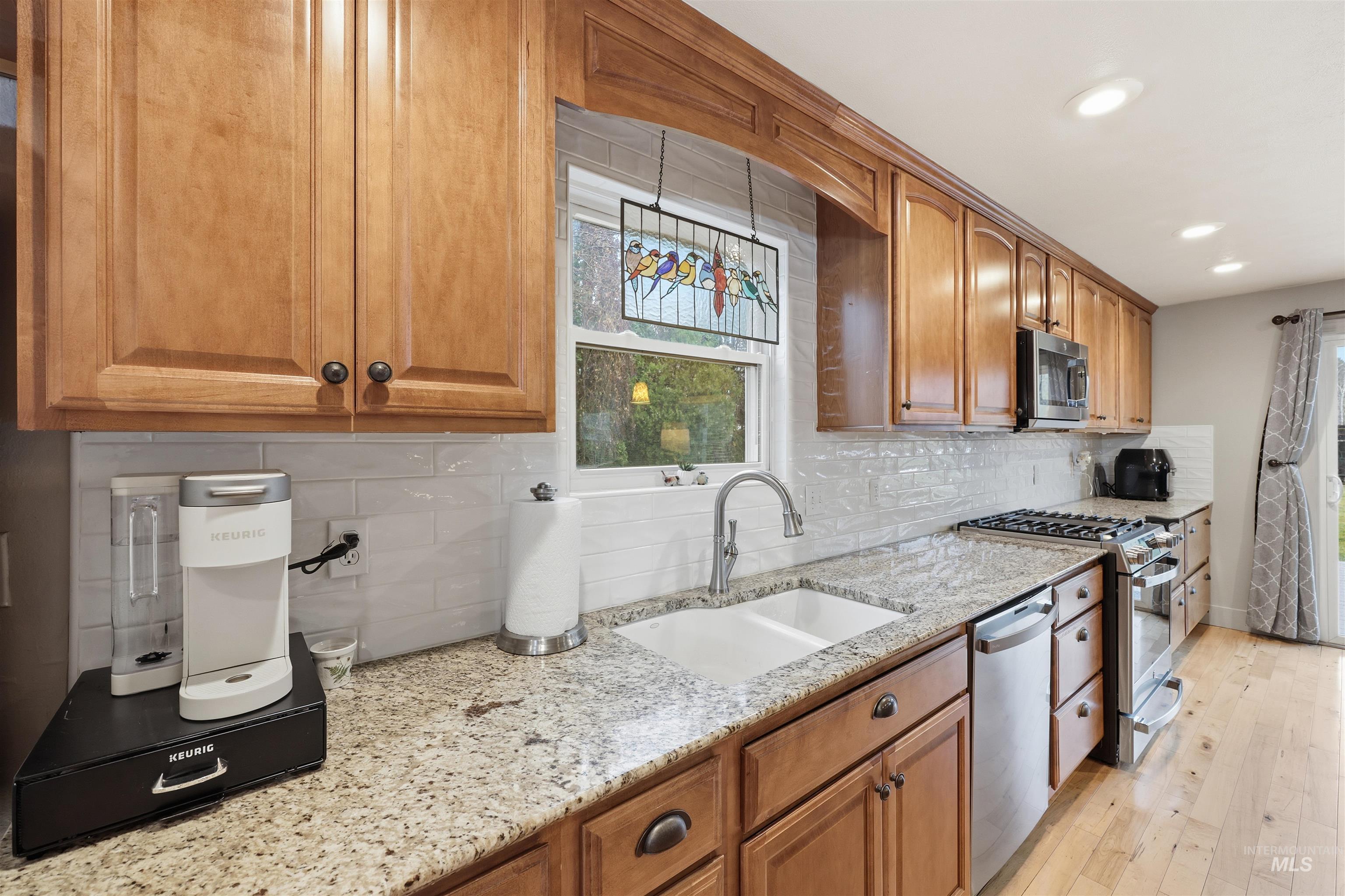 Kitchen featuring brown cabinets, light Granite counters, stainless steel appliances, decorative backsplash, and recessed lighting