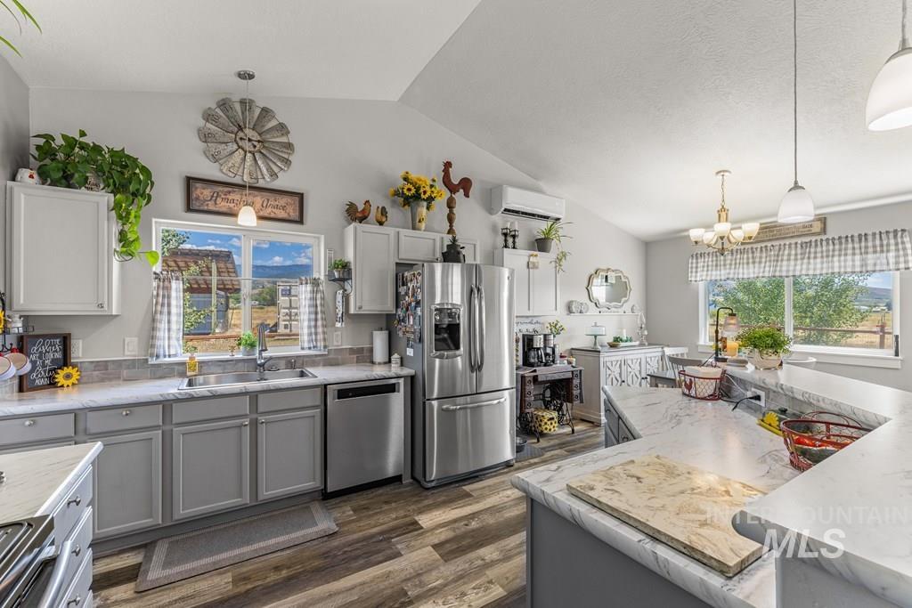 Kitchen with gray cabinets, pendant lighting, appliances with stainless steel finishes, dark wood-type flooring, and vaulted ceiling