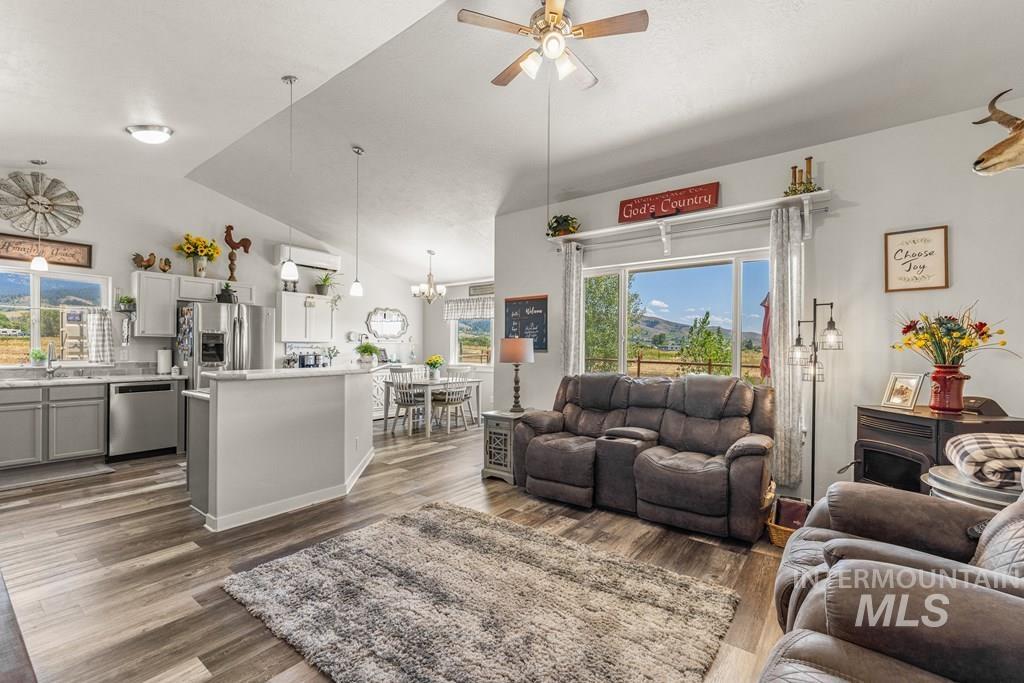 Living room featuring dark wood-style flooring, lofted ceiling, ceiling fan, a chandelier, and a wall mounted AC